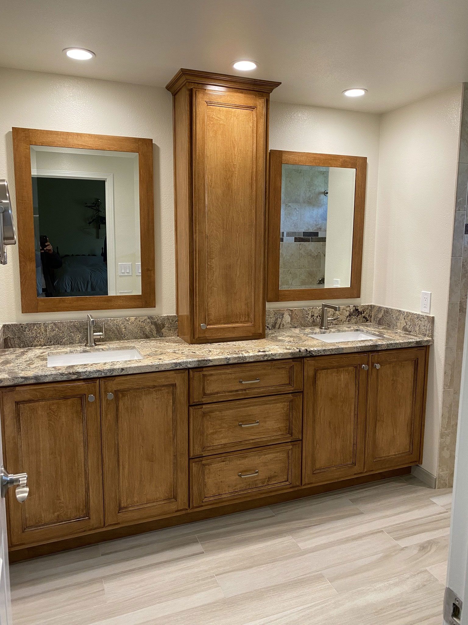 Bathroom vanity with wooden cabinets, granite countertop, two mirrors, and a tall central cabinet.