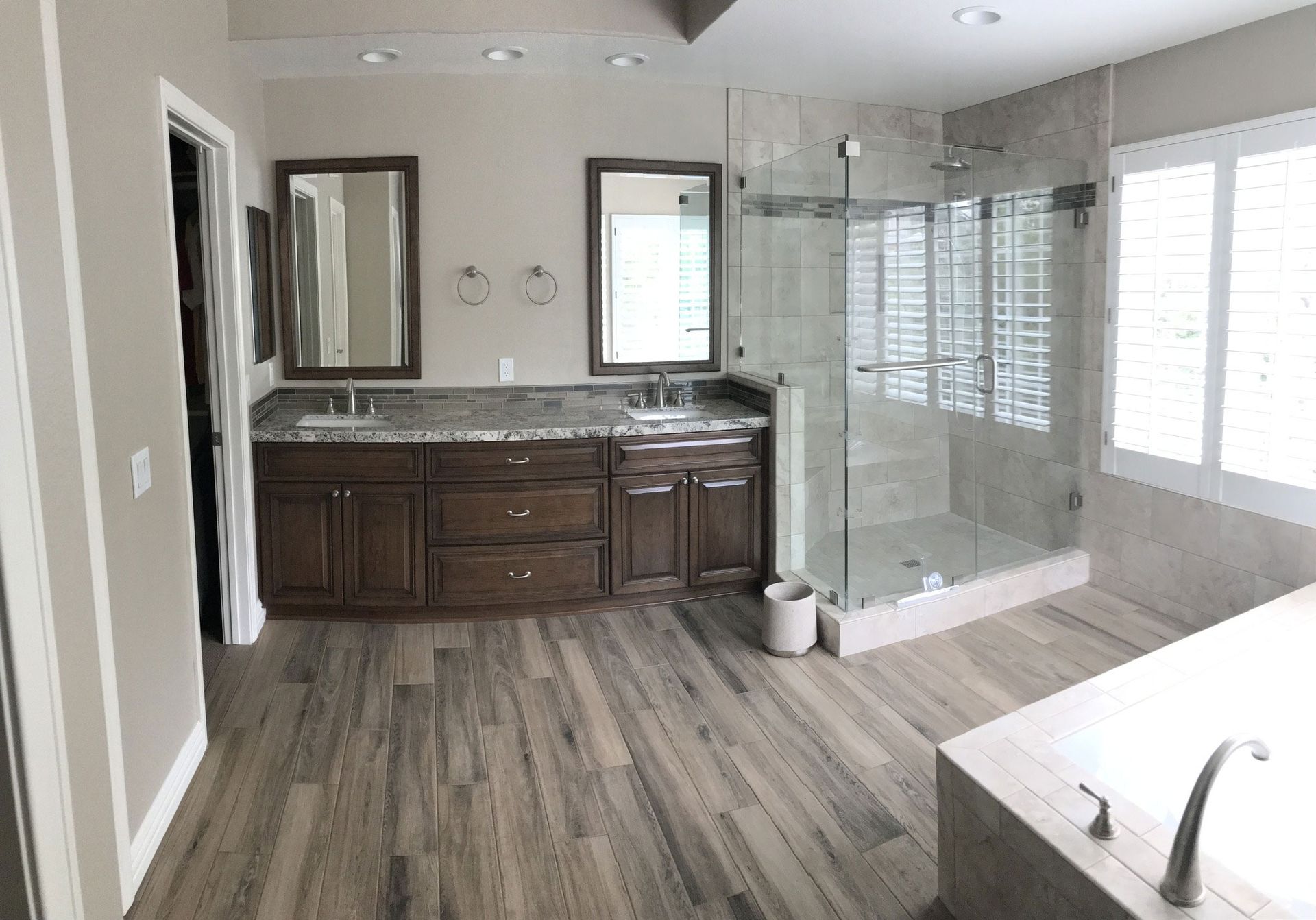 Spacious bathroom with wooden floors, double vanity, glass shower, and tub.