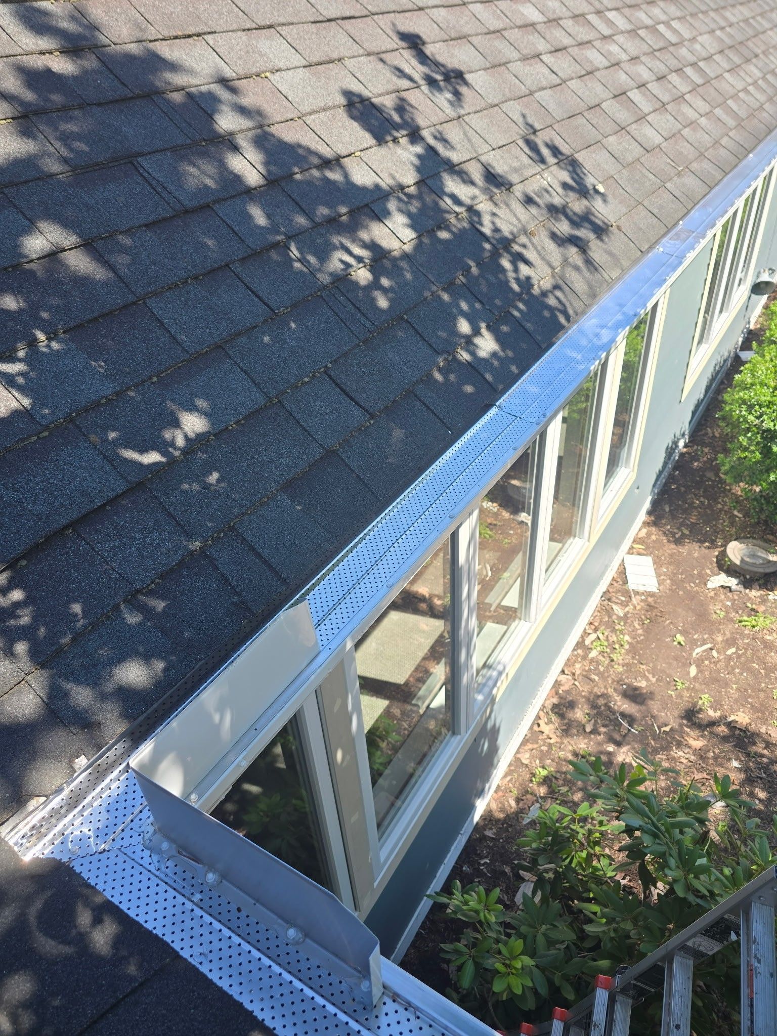 Top-down view of a shingle roofed corner with gutter guards installed.