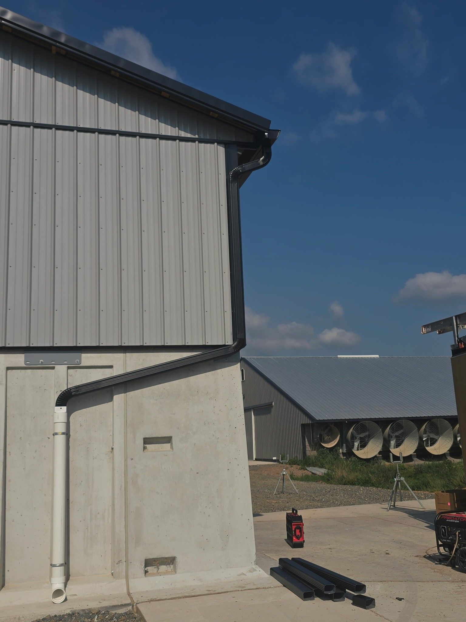 Exterior of a gray building with pipes, a red fire extinguisher, and stacked black materials on concrete under a blue sky