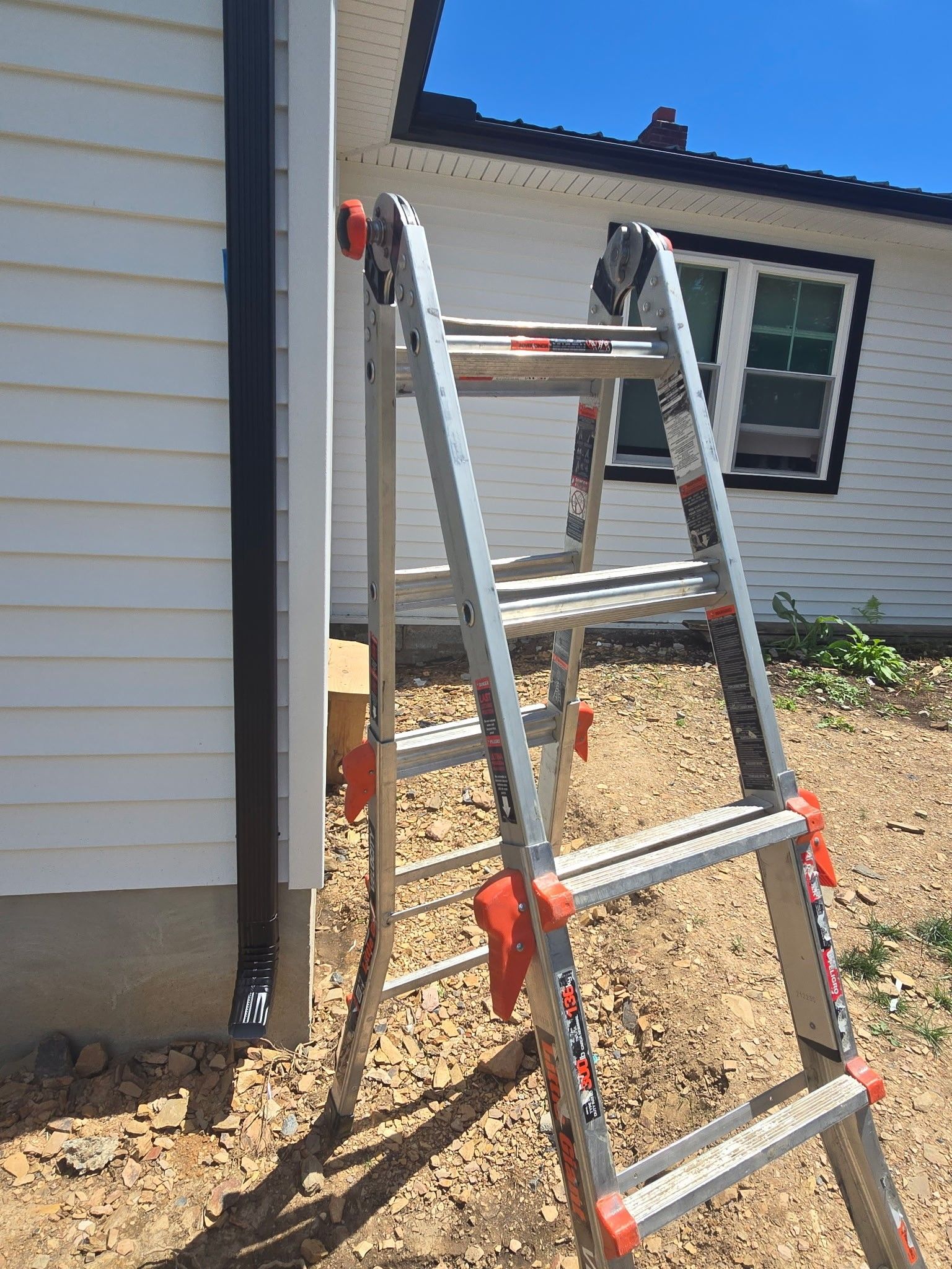 Aluminum ladder leaning against a house wall beside a window and dirt ground