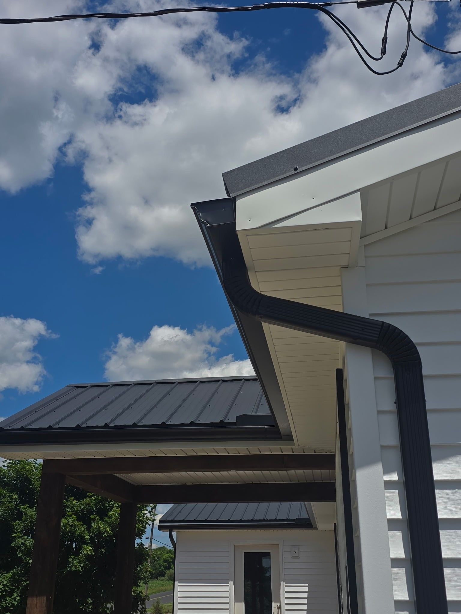 House eaves and black rain gutter against a blue sky with clouds