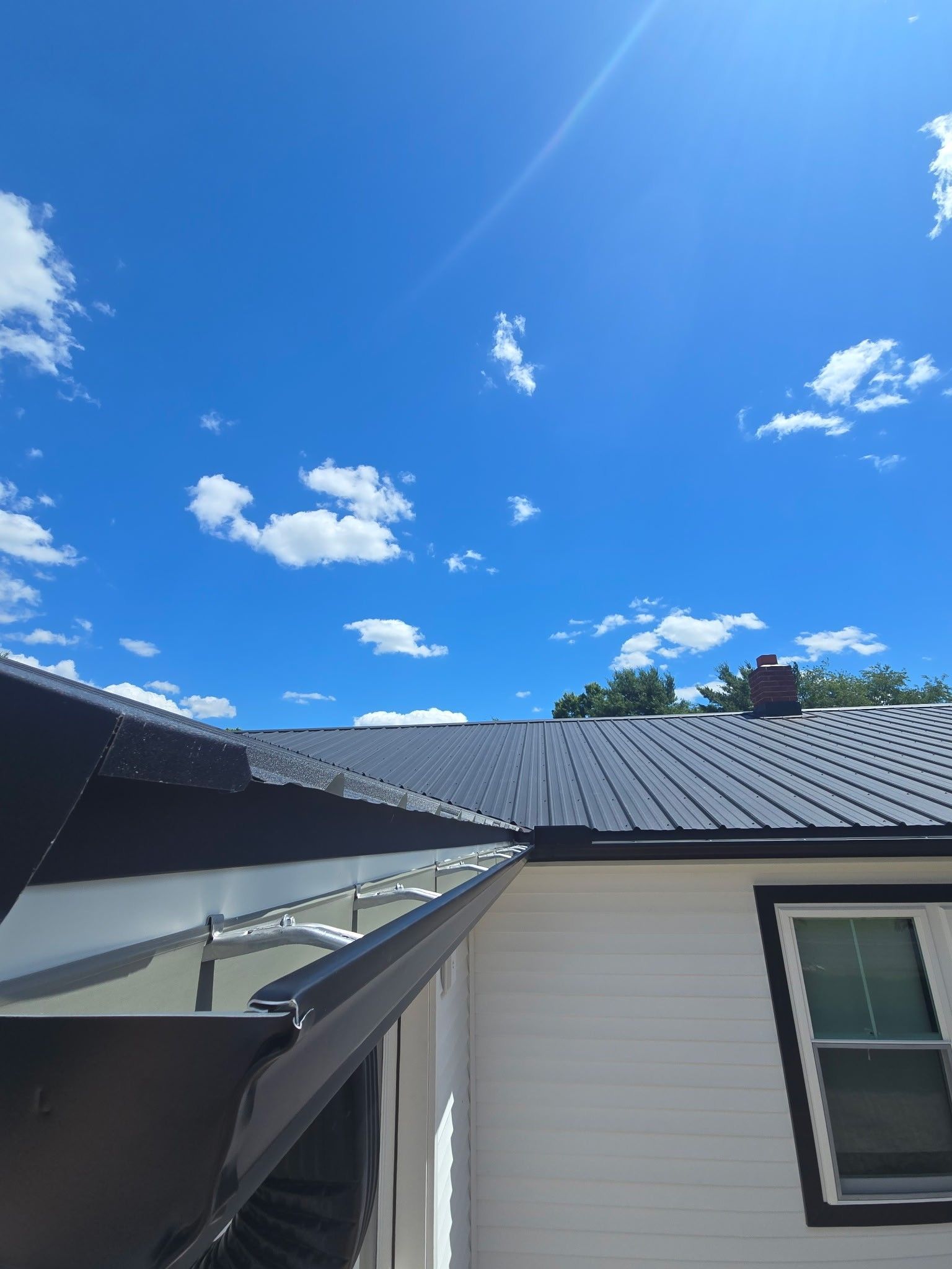 Blue sky over a white house roof with a black awning and a small rooftop vent.
