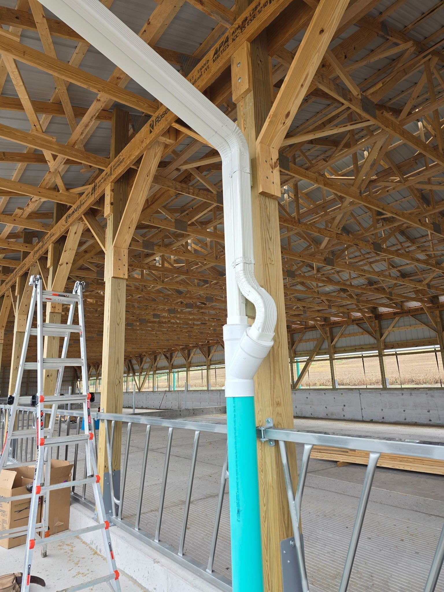 White ductwork and a turquoise pipe under a wooden barn roof, with a ladder nearby.