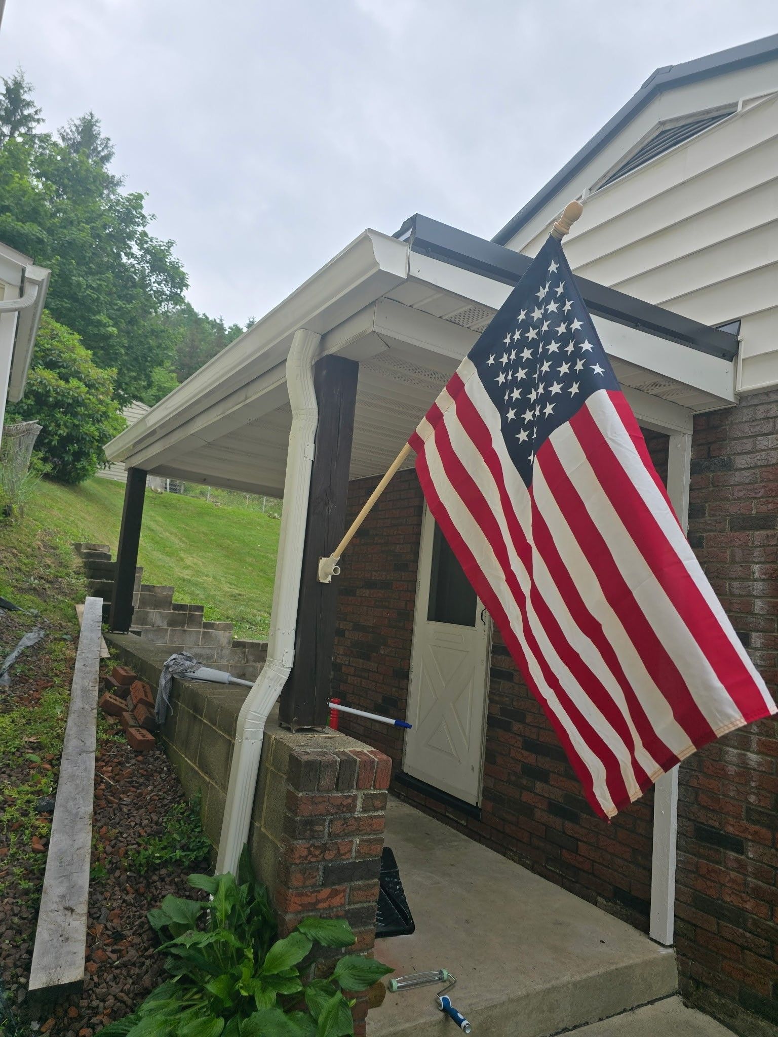 Front porch with a large American flag hanging beside a brick entryway and white siding.