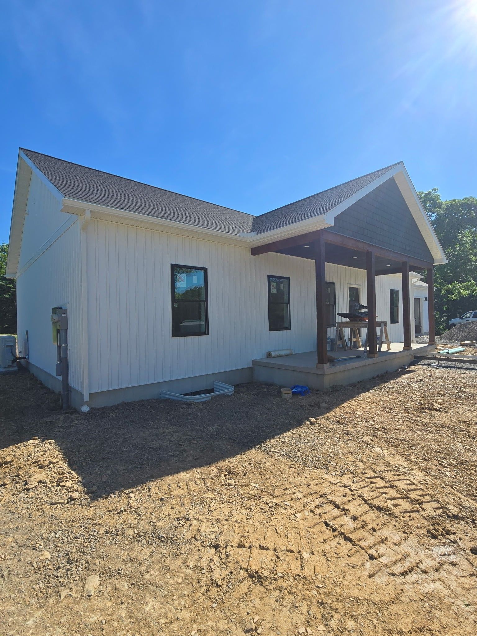 New white house exterior with dark roof and porch under a bright blue sky