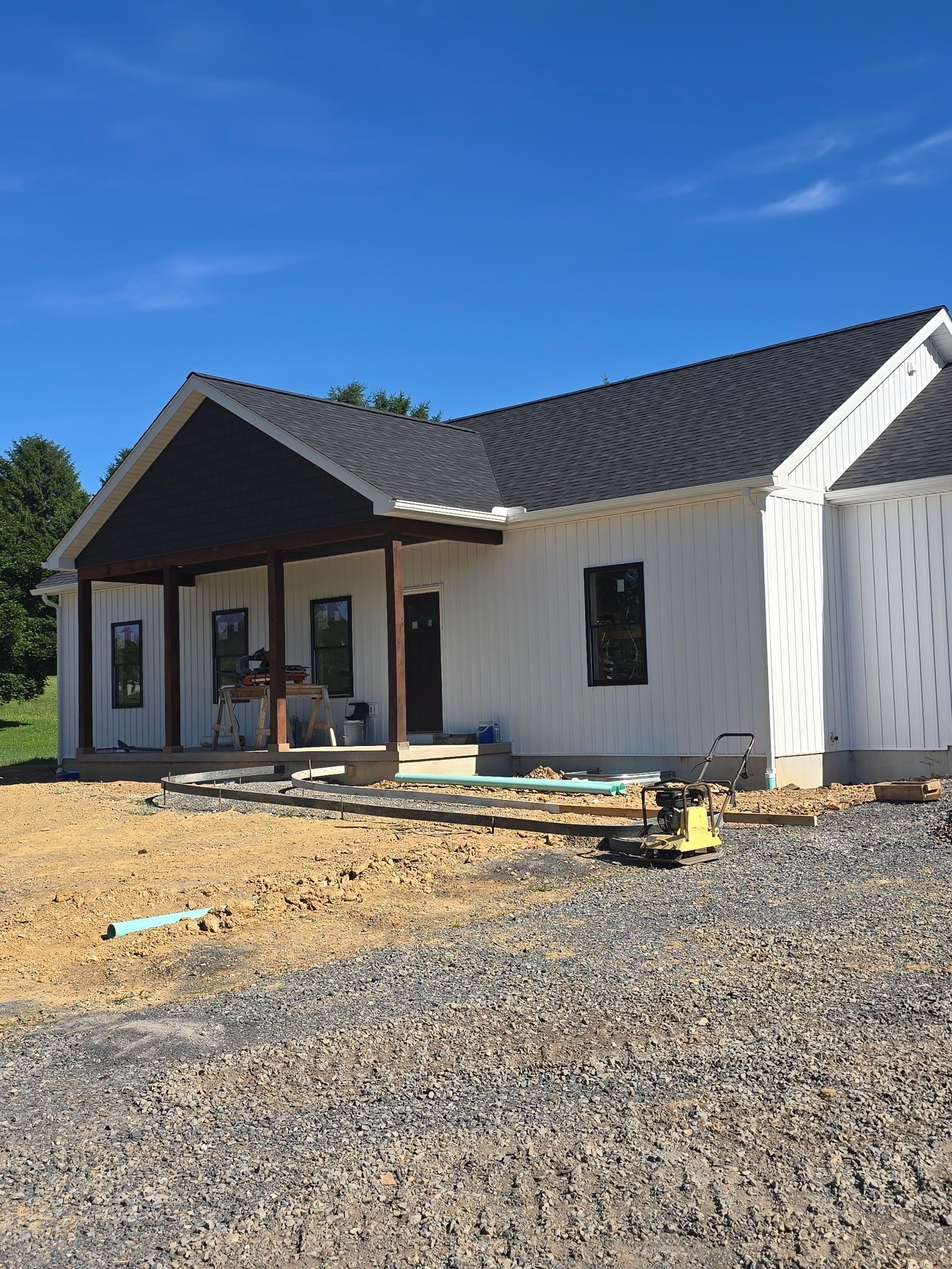 Single-story house under construction with a front porch, gravel yard, and blue sky.