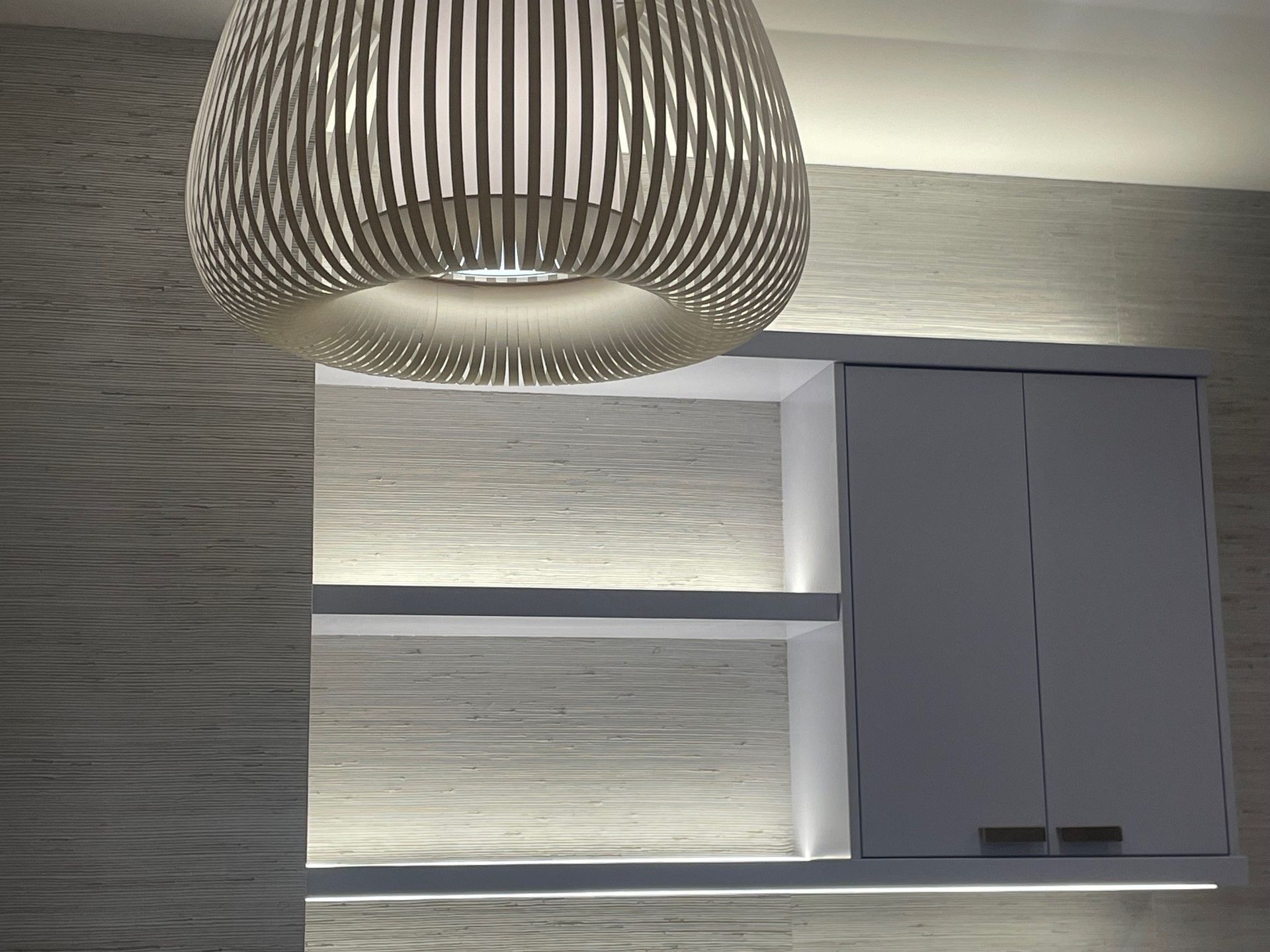 A modern light fixture hangs above a built-in cabinet with shelves and lighting.