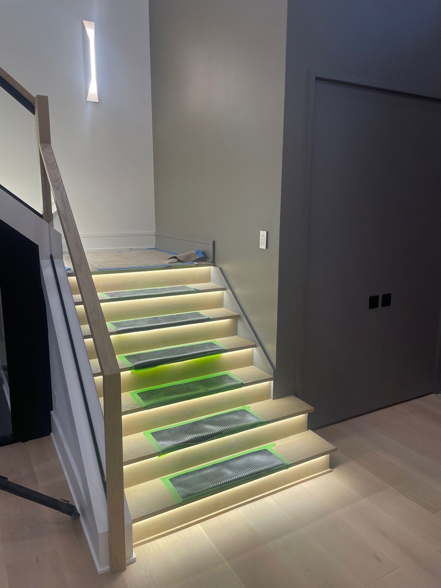 Staircase with wood steps and ledges, lit from below.  A wooden railing is on the left, and a dark door is on the right.