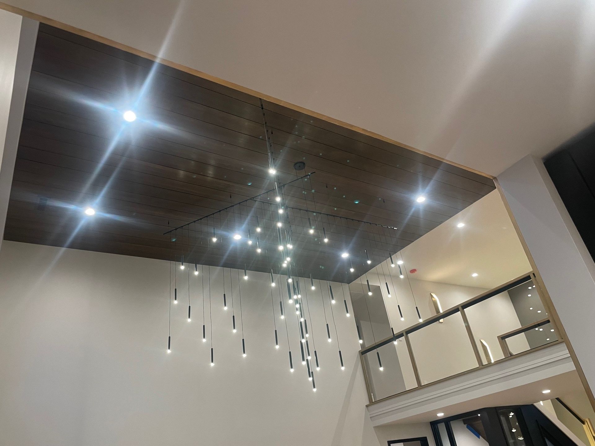 Modern room: dark wood ceiling with hanging lights, white walls, and a balcony.