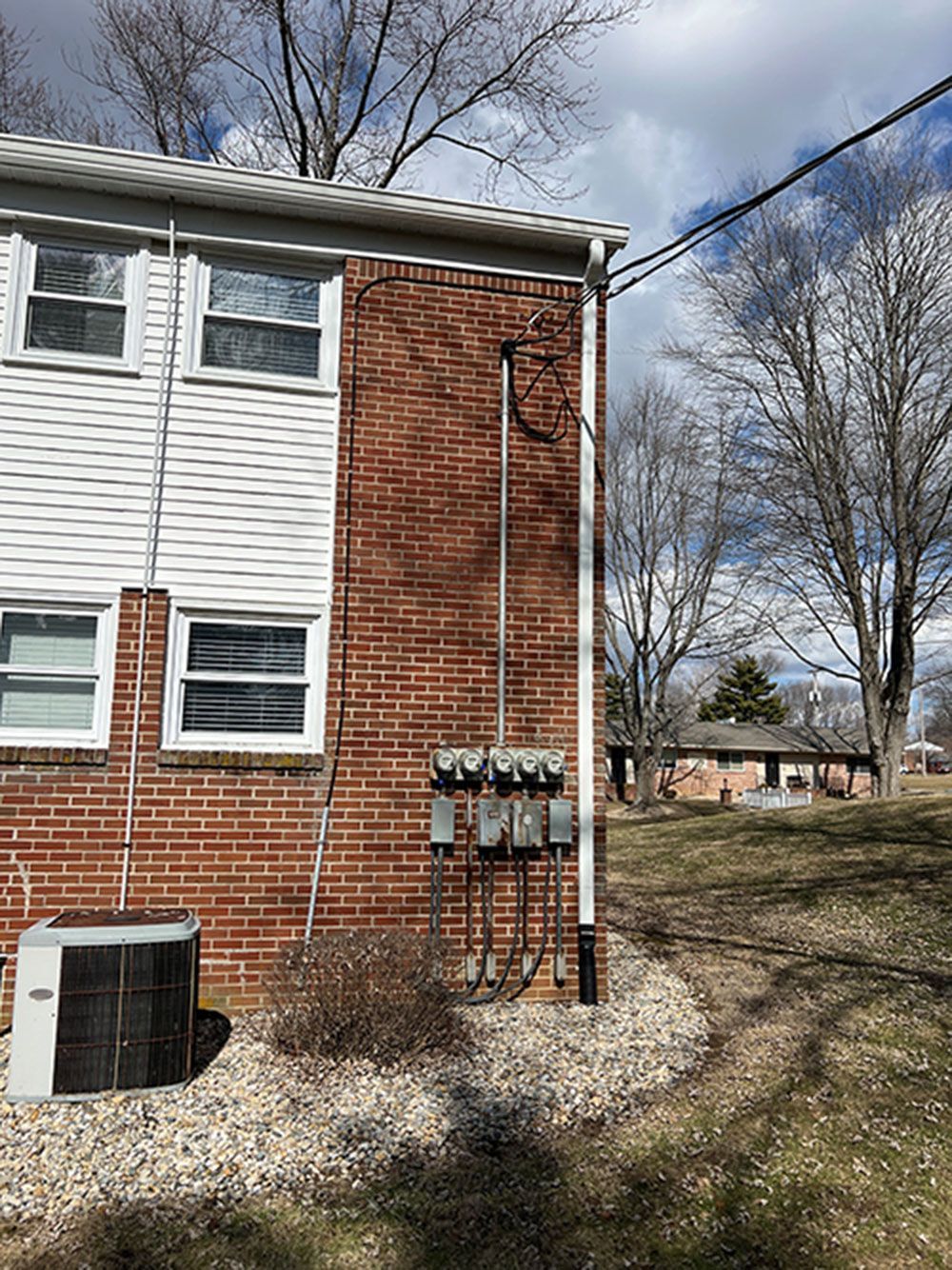 Brick building exterior with power meters, utility lines, and bare trees on a sunny day.