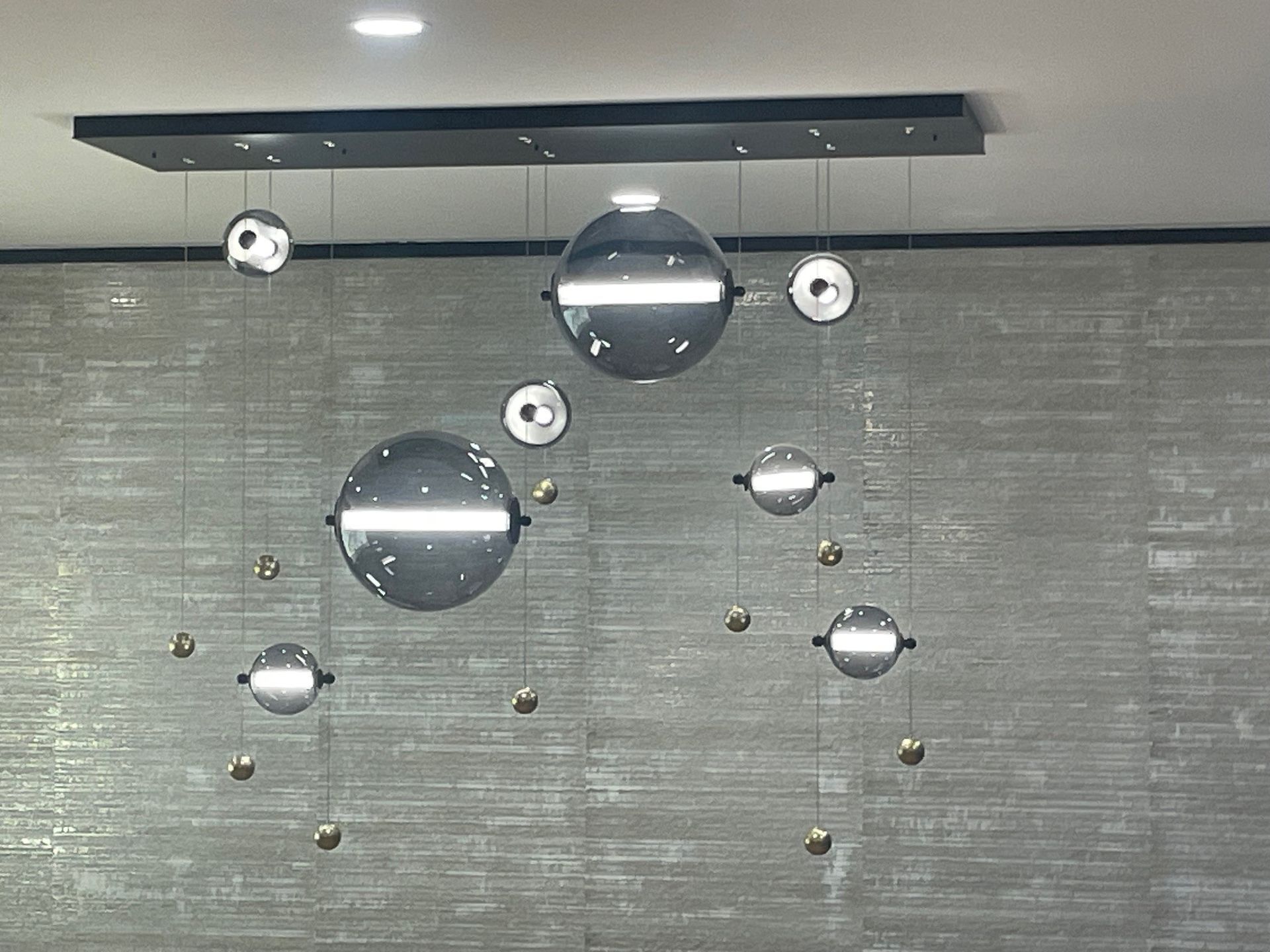 Modern chandelier with reflective spheres hanging from a rectangular fixture against a textured wall.
