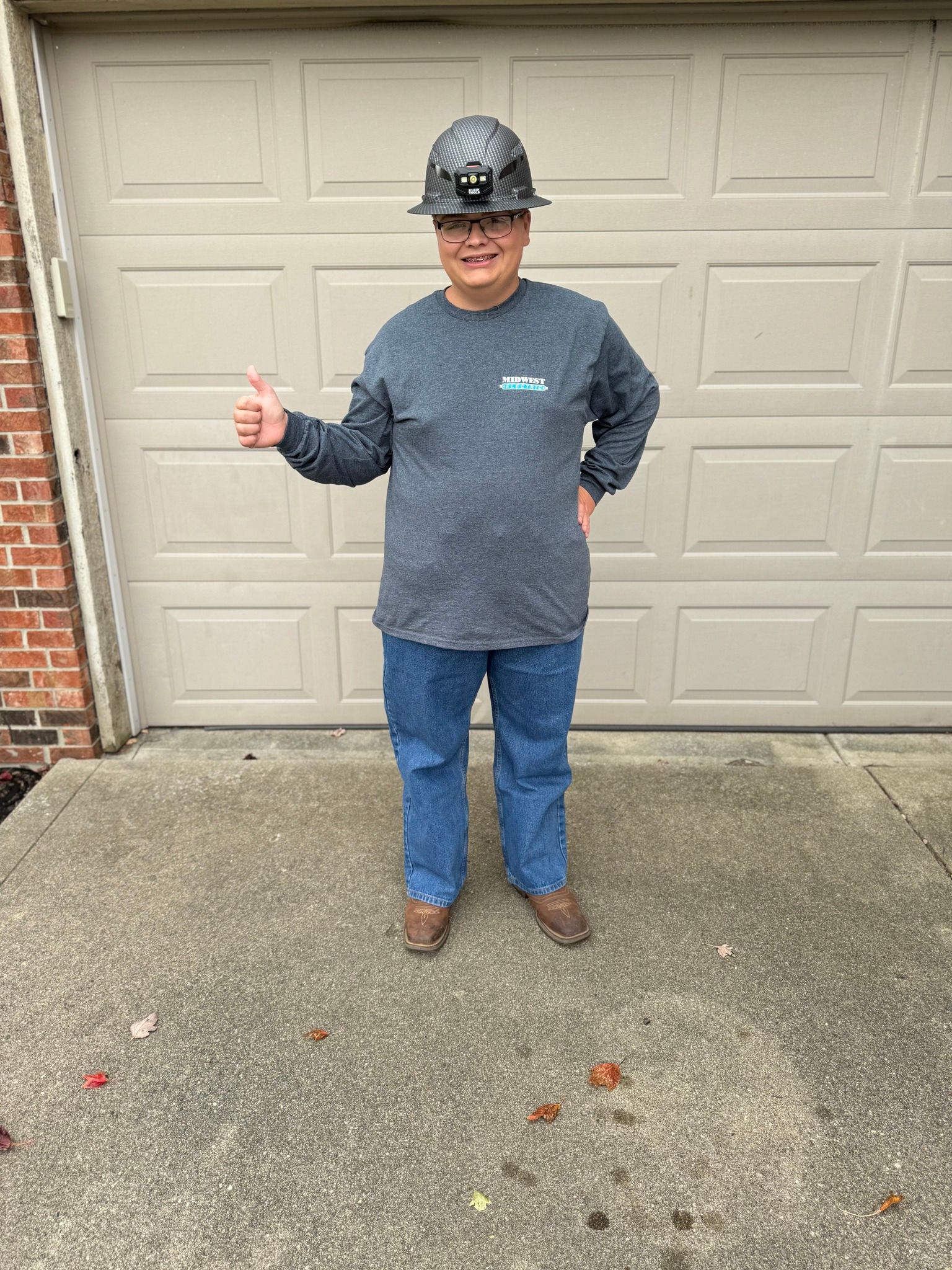 Man in work clothes and hard hat giving a thumbs up in front of a garage door.