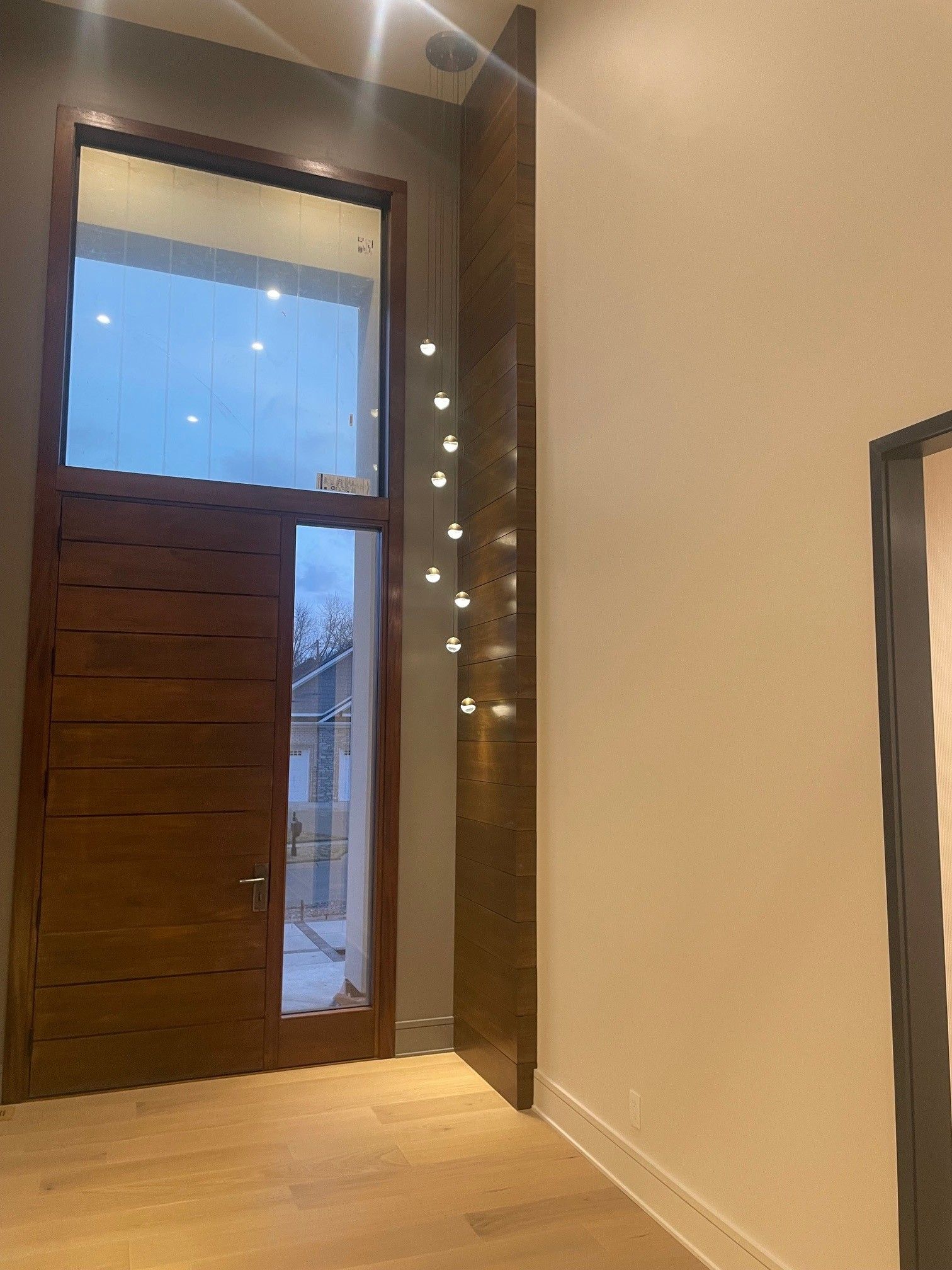 Wooden door with sidelight, interior hallway, light colored walls, and wood floor.