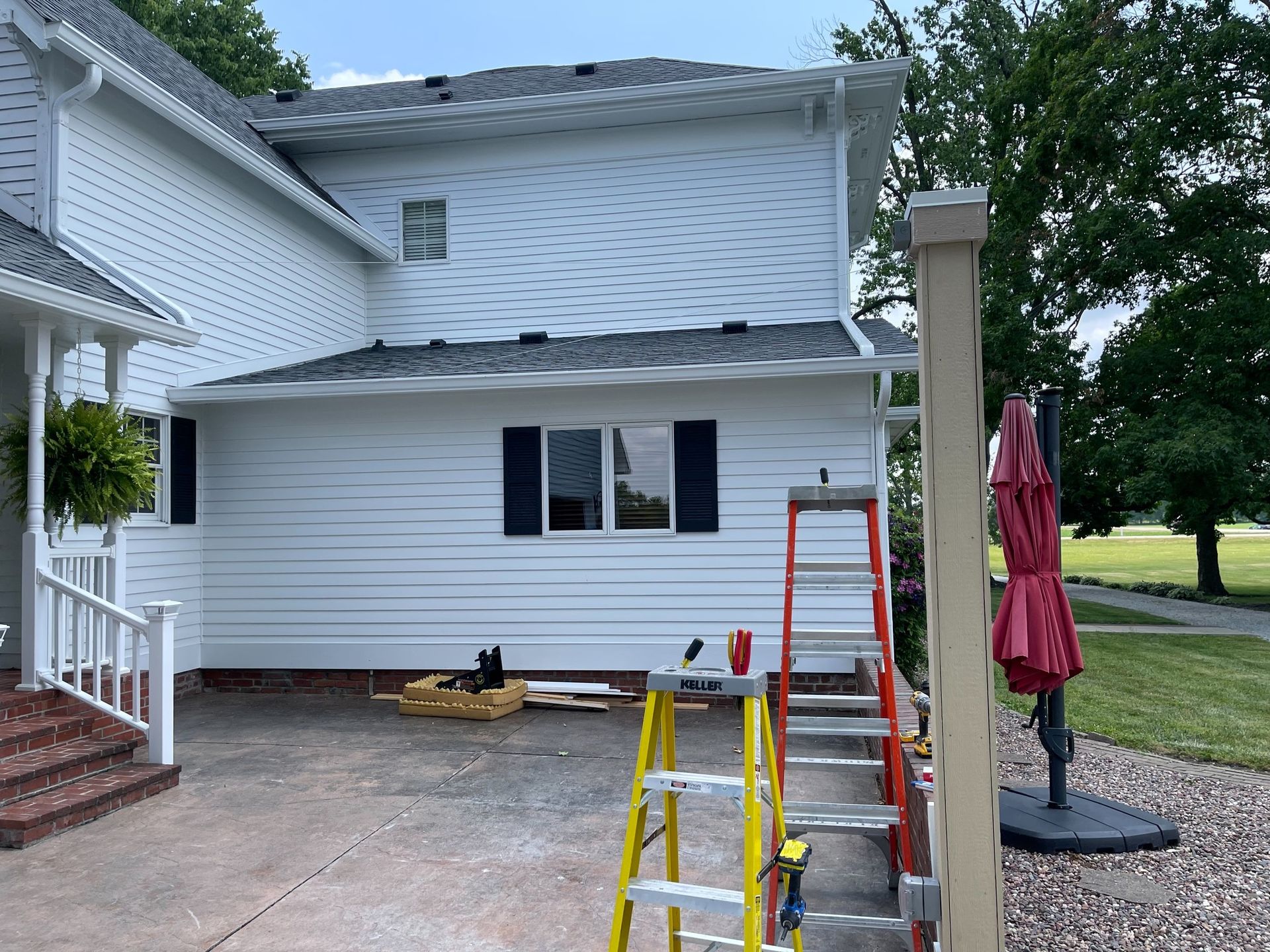 White house with siding being worked on; ladders, tools, and umbrella visible.