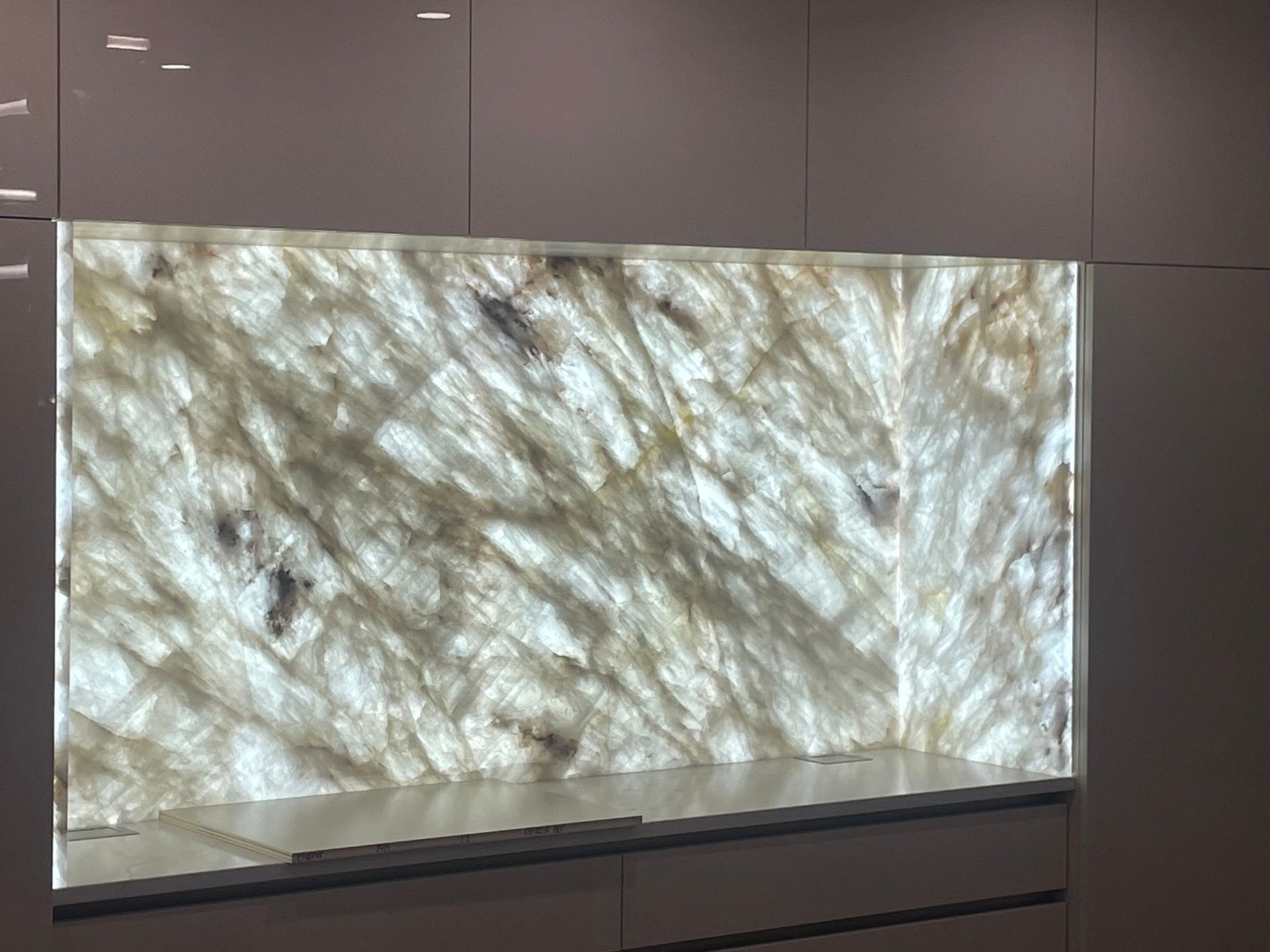 Backlit translucent marble panel mounted on a wall, displaying swirling light and dark patterns.