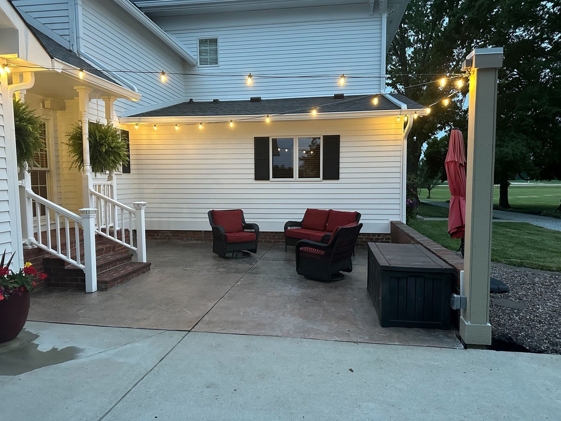Patio with red furniture, string lights, white building, and green space.