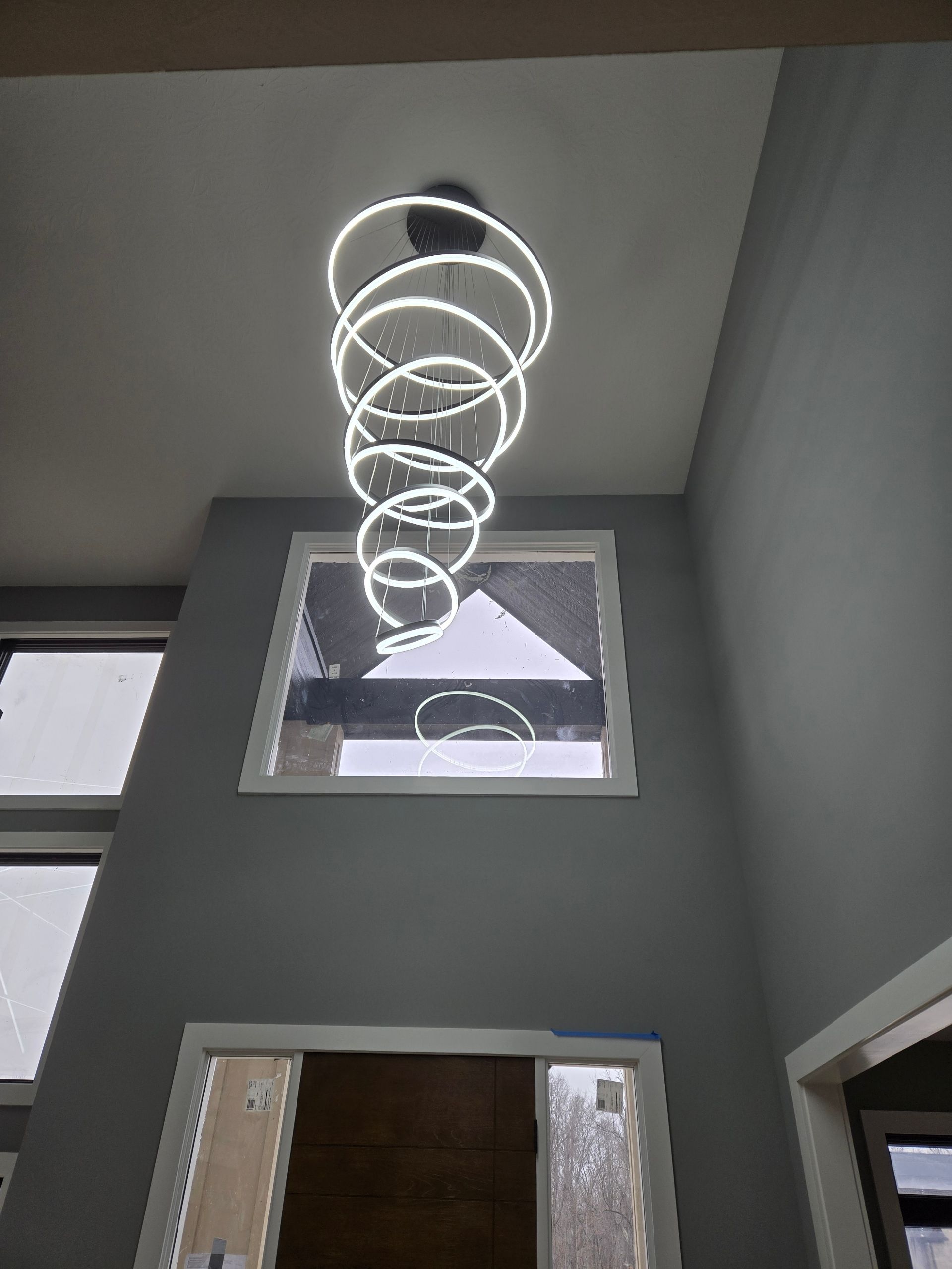 Modern spiral chandelier in a gray-walled foyer, above a window.