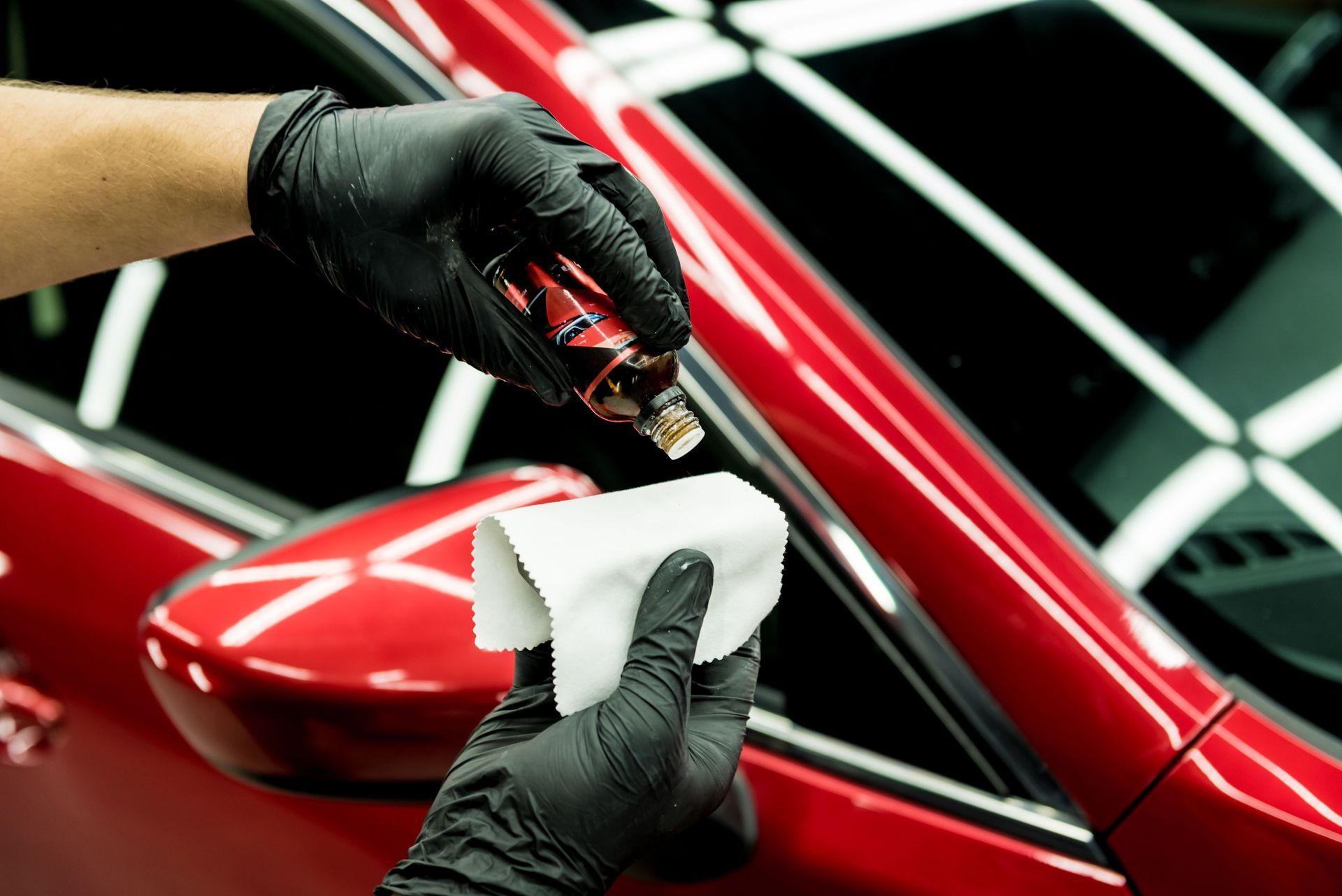 Gloved hands polishing a red car’s side mirror with a white cloth.