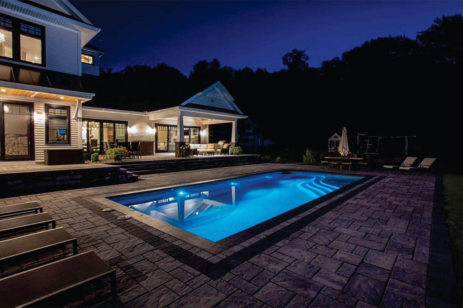 a large swimming pool is lit up at night in front of a house