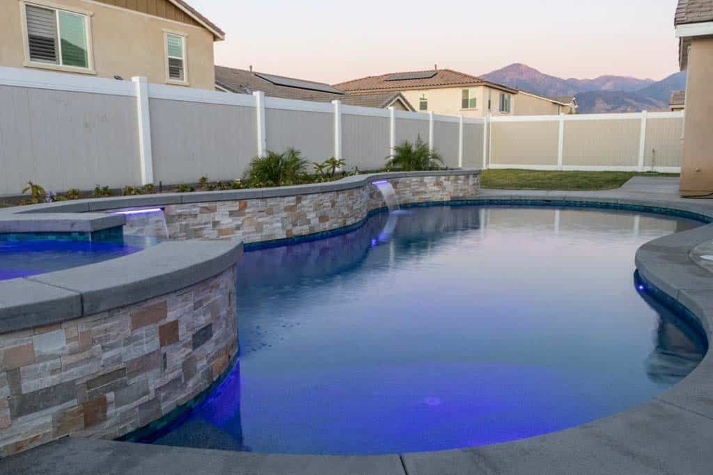 a large swimming pool in a backyard with a white fence and mountains in the background