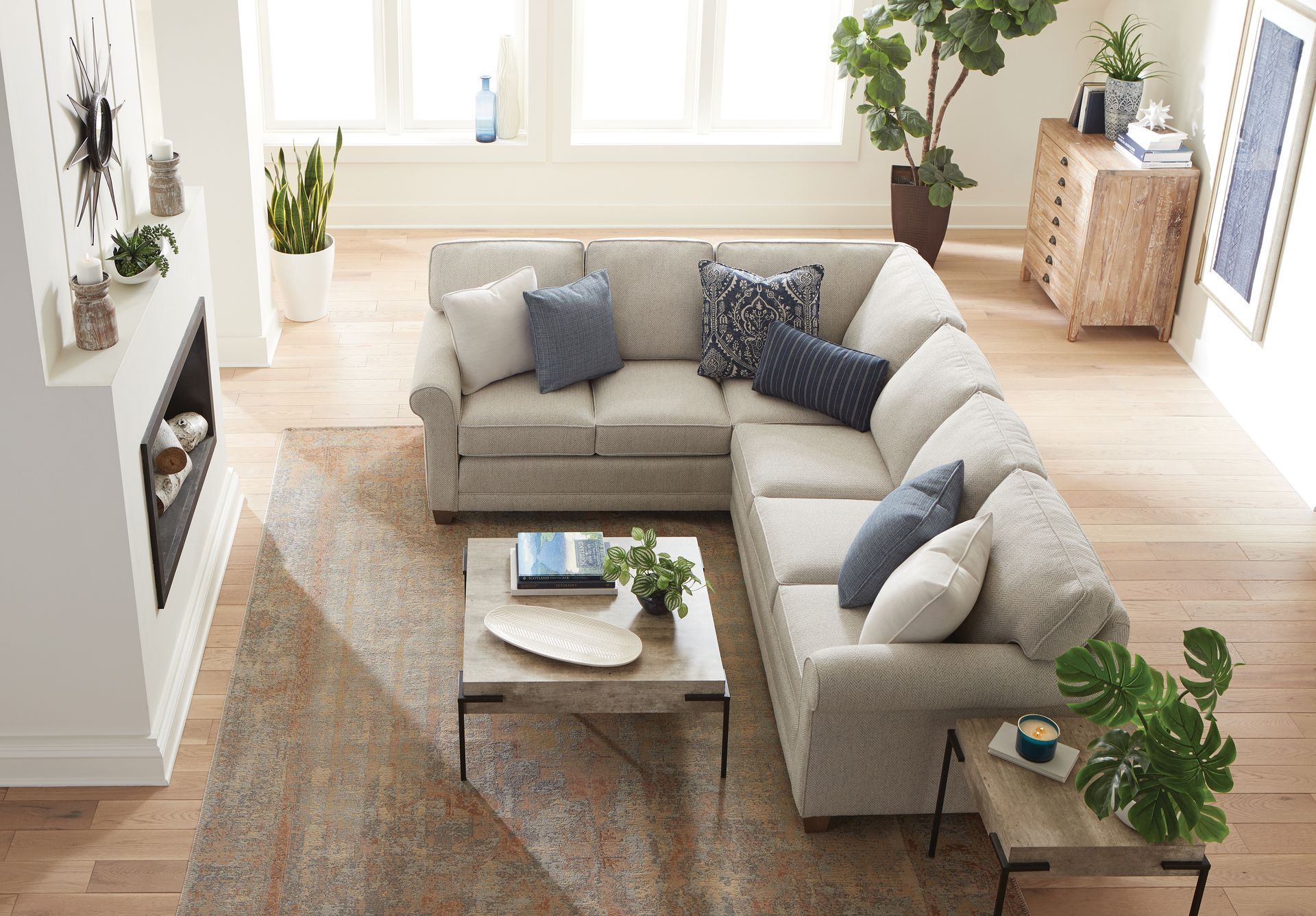L-shaped beige sectional sofa in a bright living room with a rug, coffee table, and fireplace.