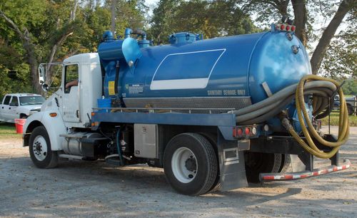 Blue vacuum truck parked outdoors with hoses coiled on the back