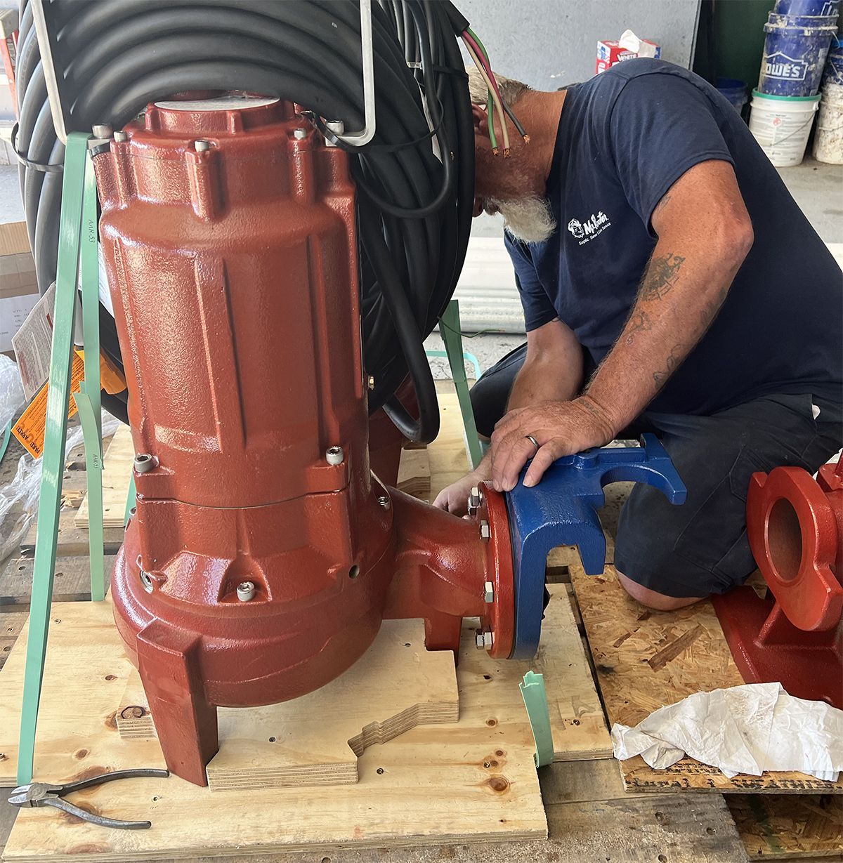 Worker installing a large red industrial pump on a wooden pallet.