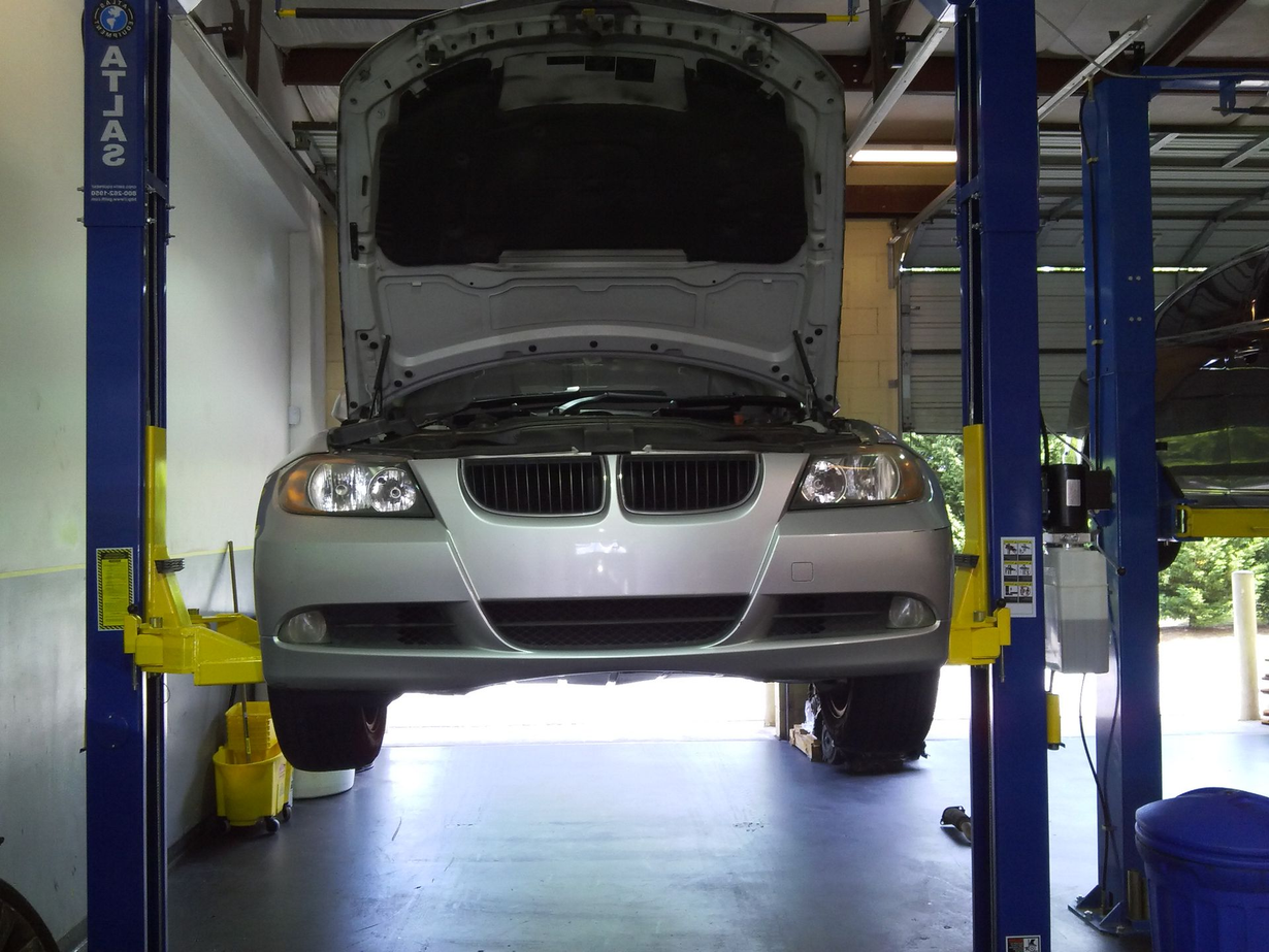 Silver car on a hydraulic lift in a garage with hood open, ready for service.