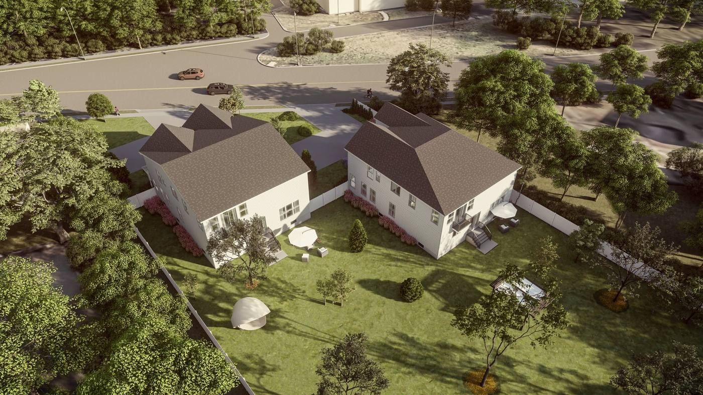 Aerial view of two white houses with dark roofs on a grassy rural property near trees and a road.