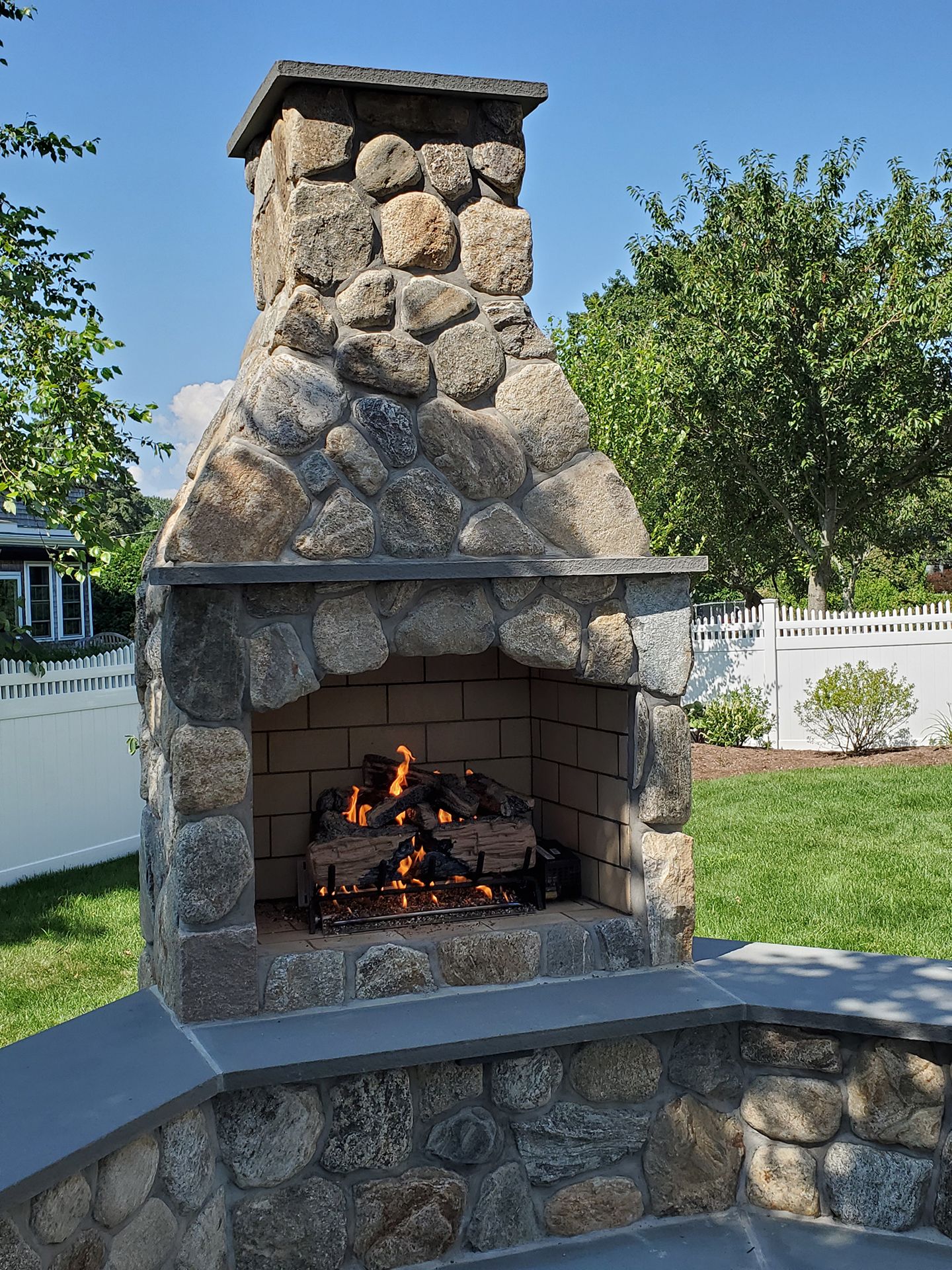 A stone fireplace is sitting in the middle of a lush green yard.