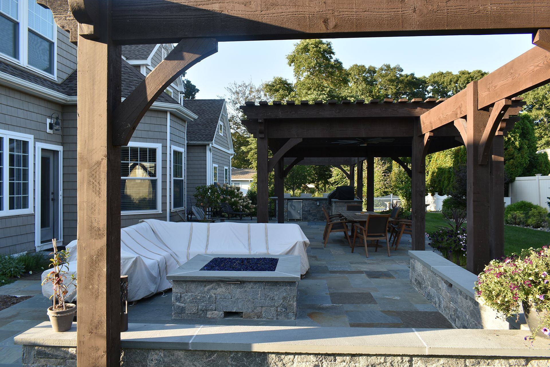There is a fire pit in the middle of the patio under a pergola.