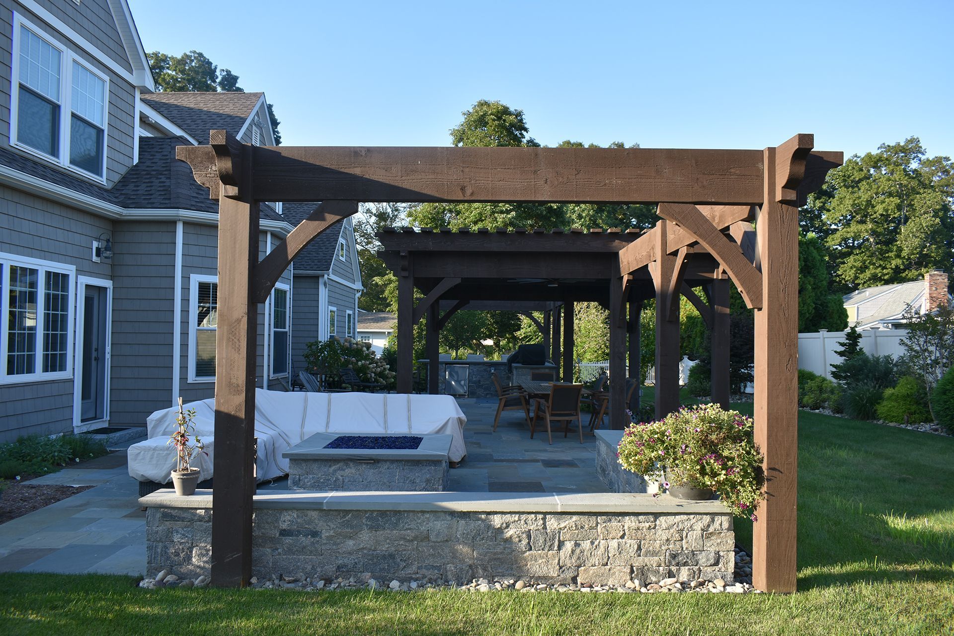 A wooden pergola with a fire pit in the backyard of a house.