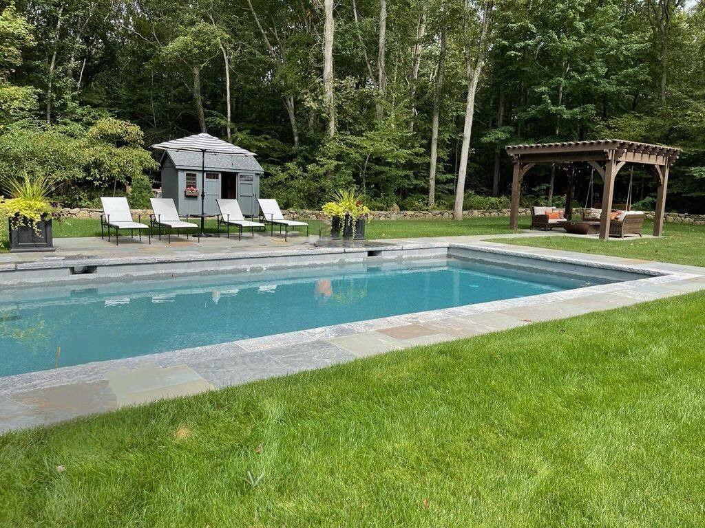 A large swimming pool in a backyard with a gazebo and chairs.