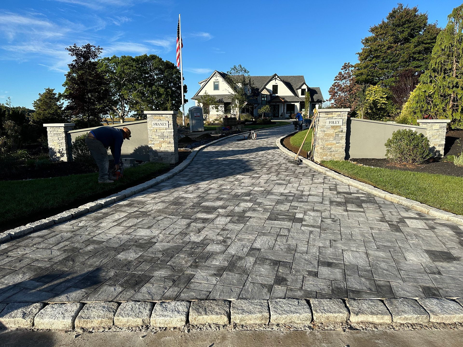 A man is working on a driveway in front of a large house.