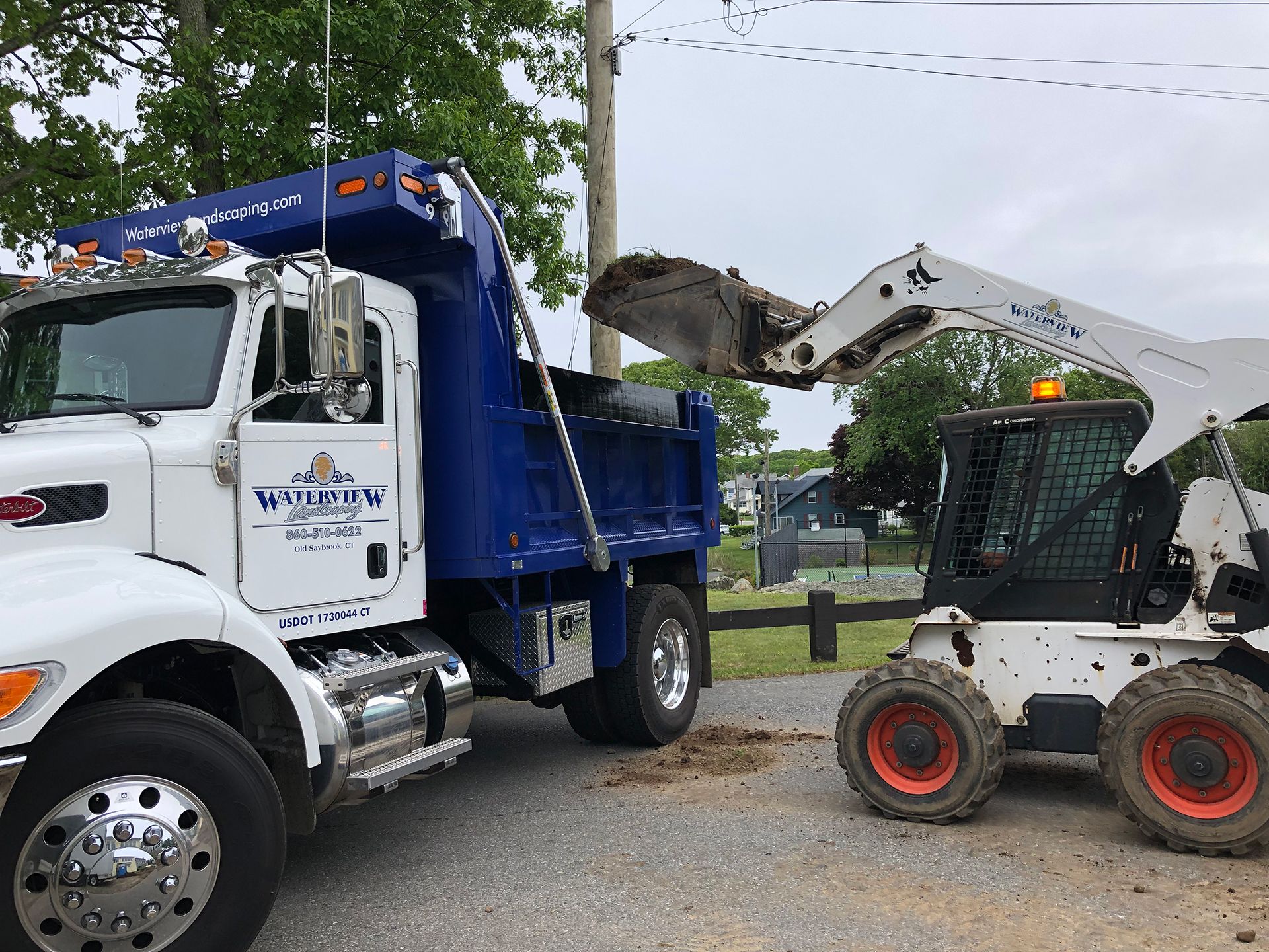 A dump truck is being loaded with dirt next to a bobcat skid steer loader.