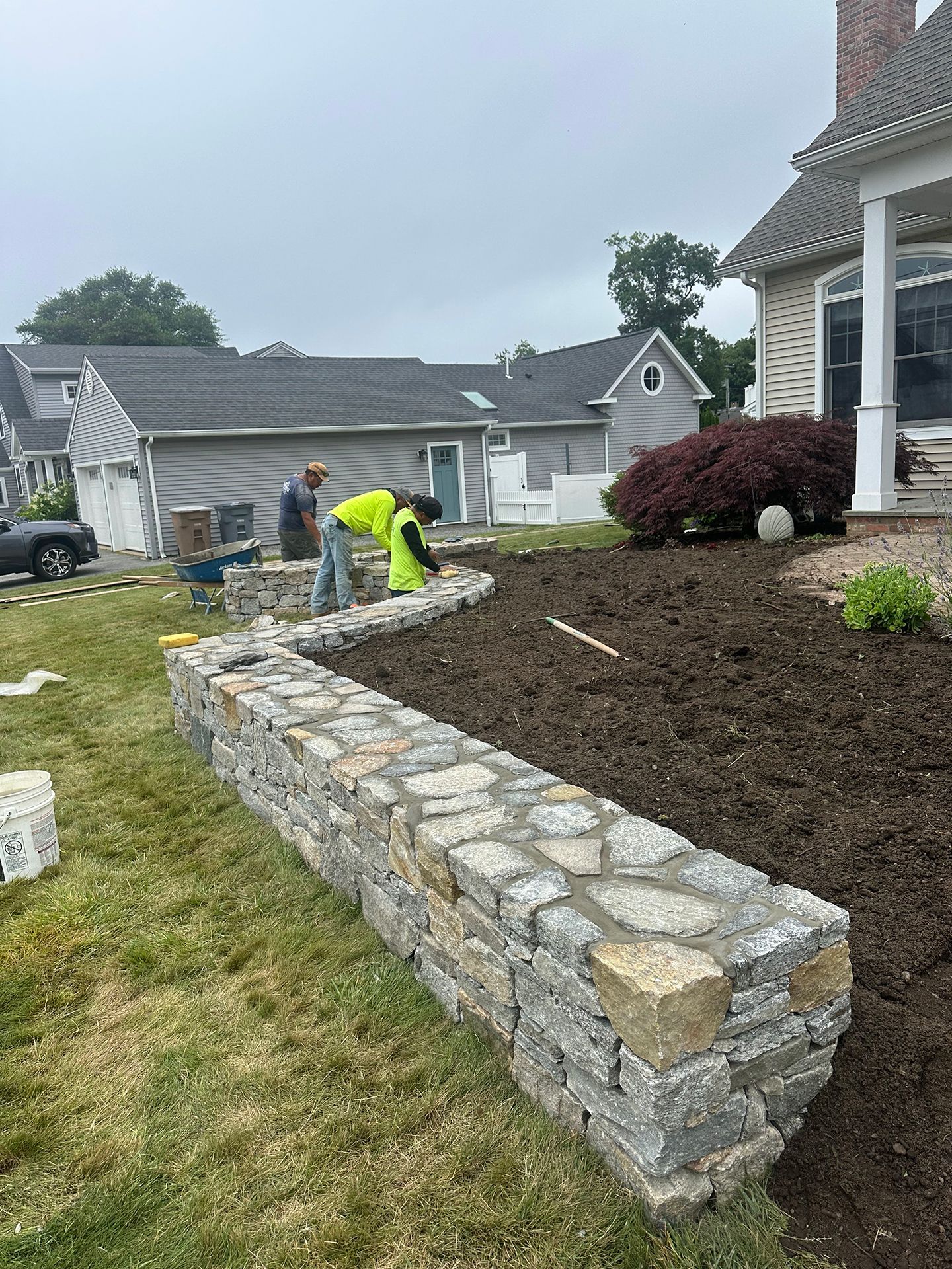 A man is working on a stone wall in front of a house.