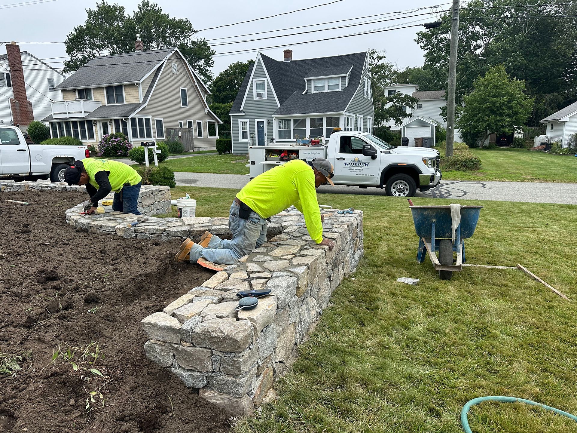 A group of men are working on a stone wall in a yard.