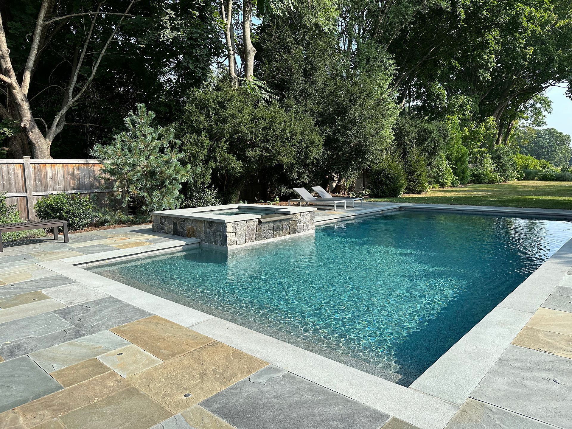 A large swimming pool is surrounded by trees and a fence.