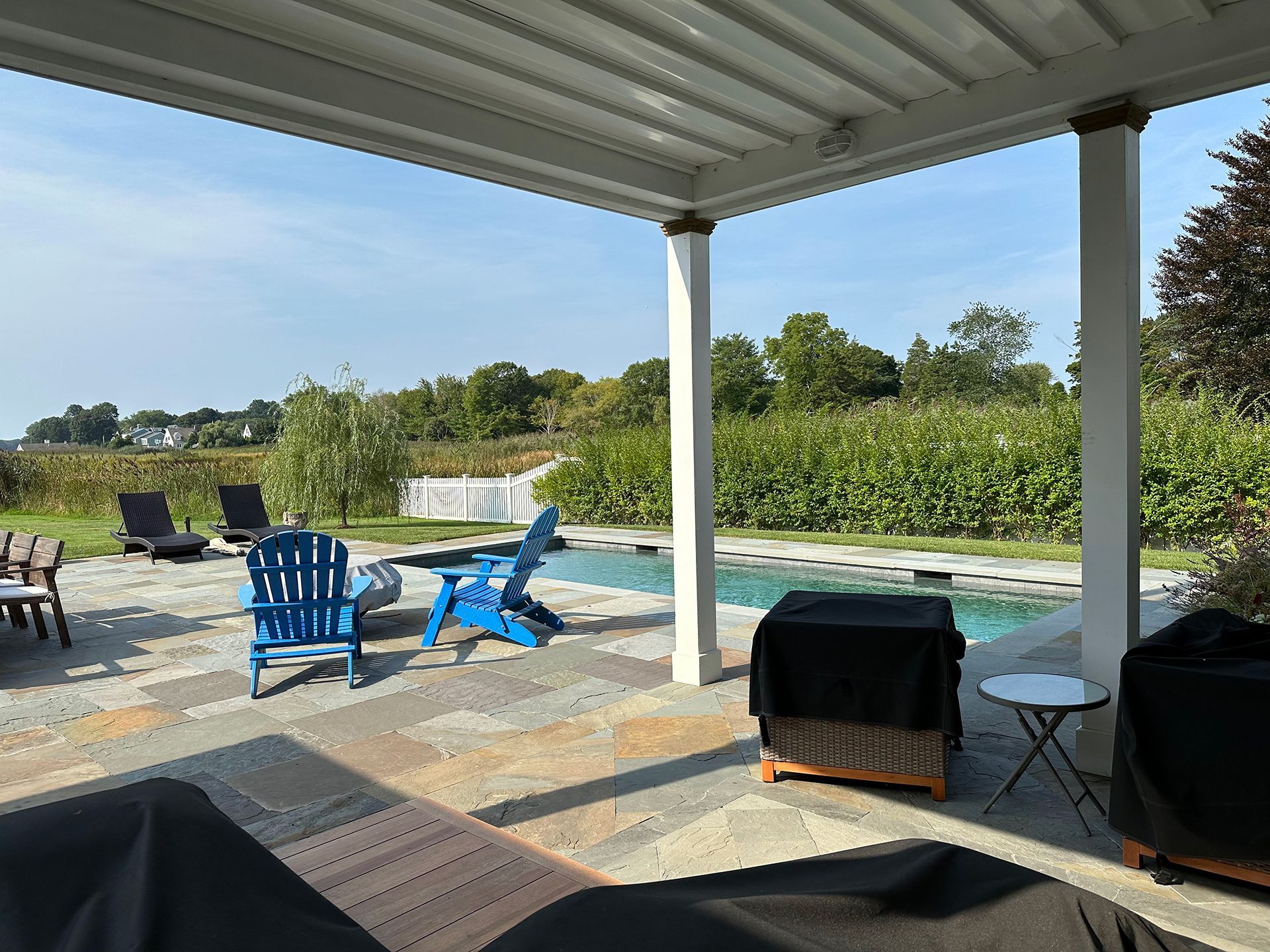 A patio with blue chairs and a swimming pool in the background.