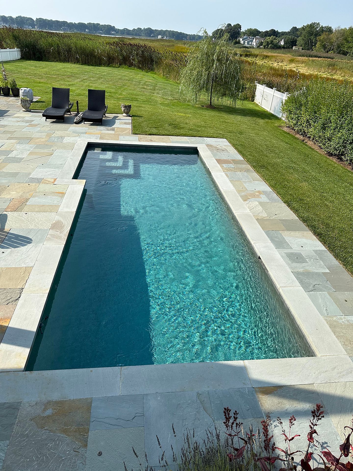 A large swimming pool is surrounded by lawn chairs and a patio.