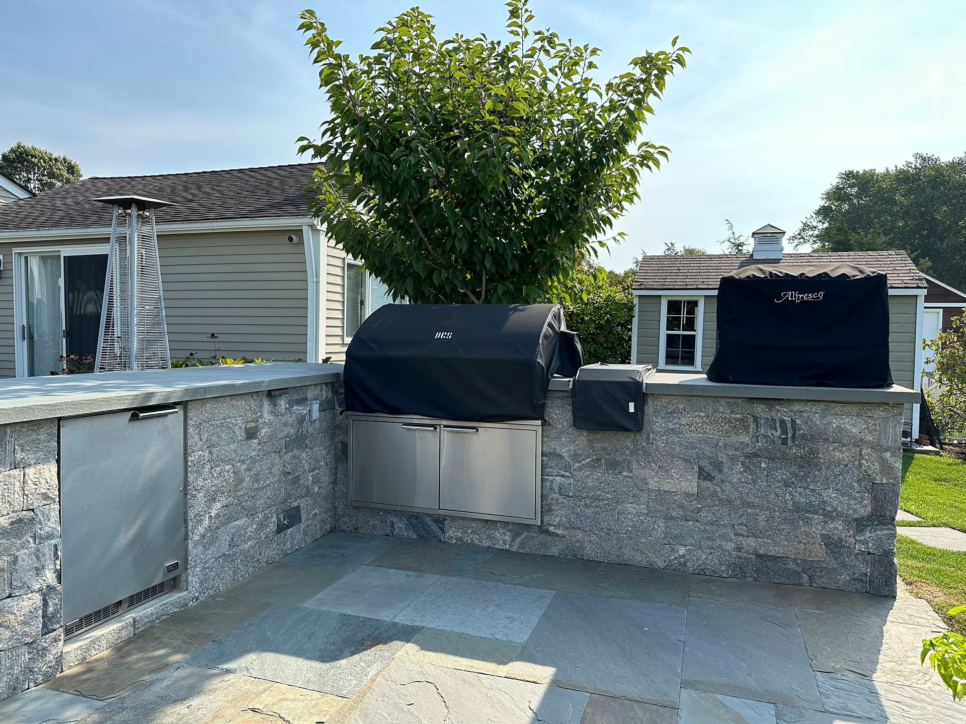 A stainless steel grill is sitting on a stone wall in front of a house.