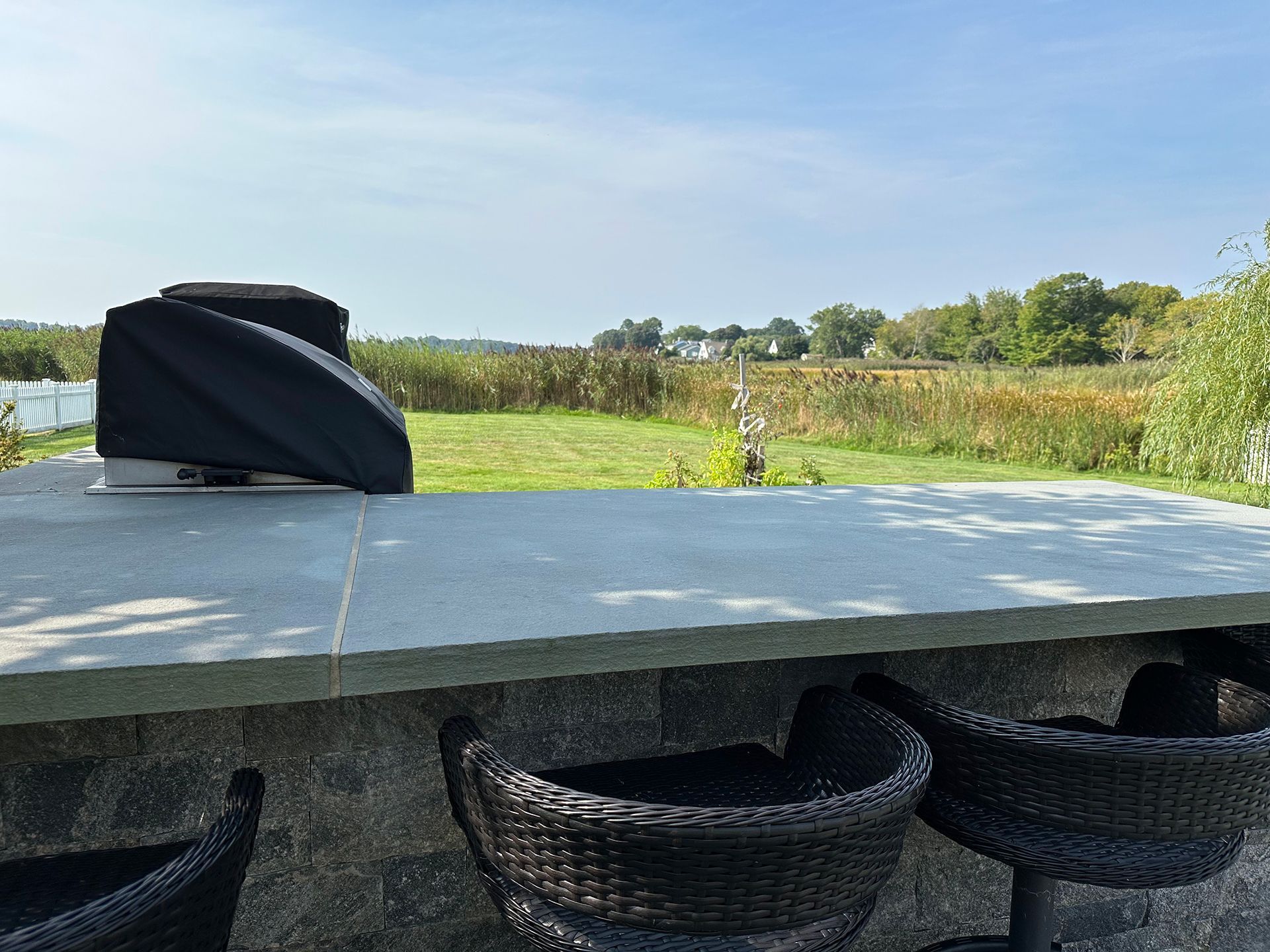 A patio with wicker chairs and a table with a view of a field.