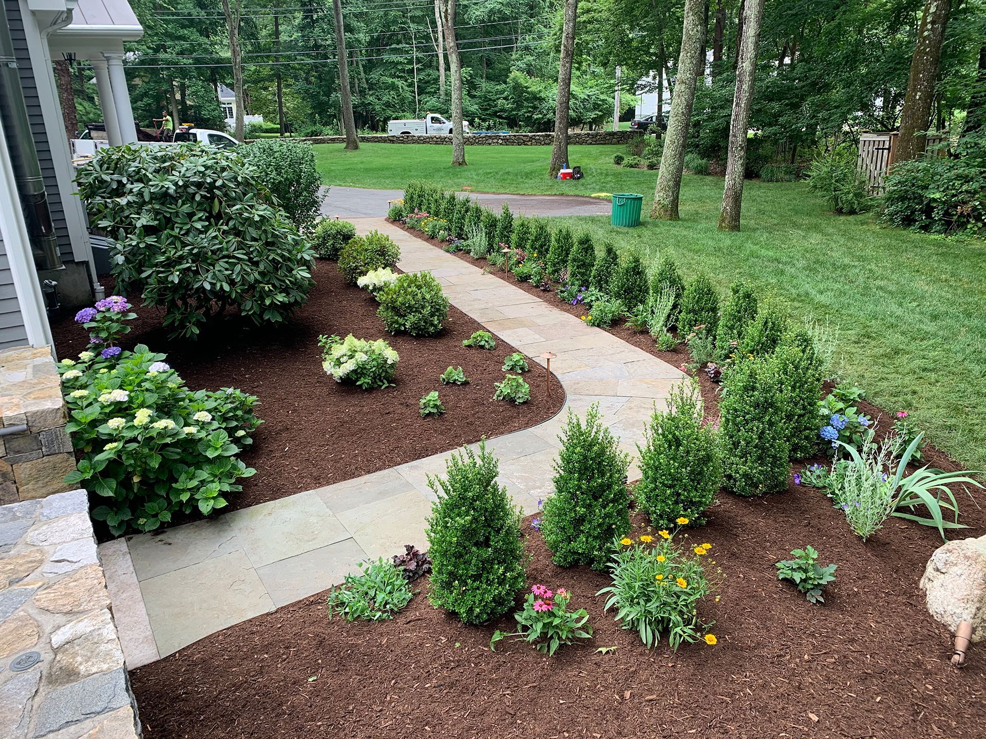 A walkway leading to a house surrounded by trees and flowers.
