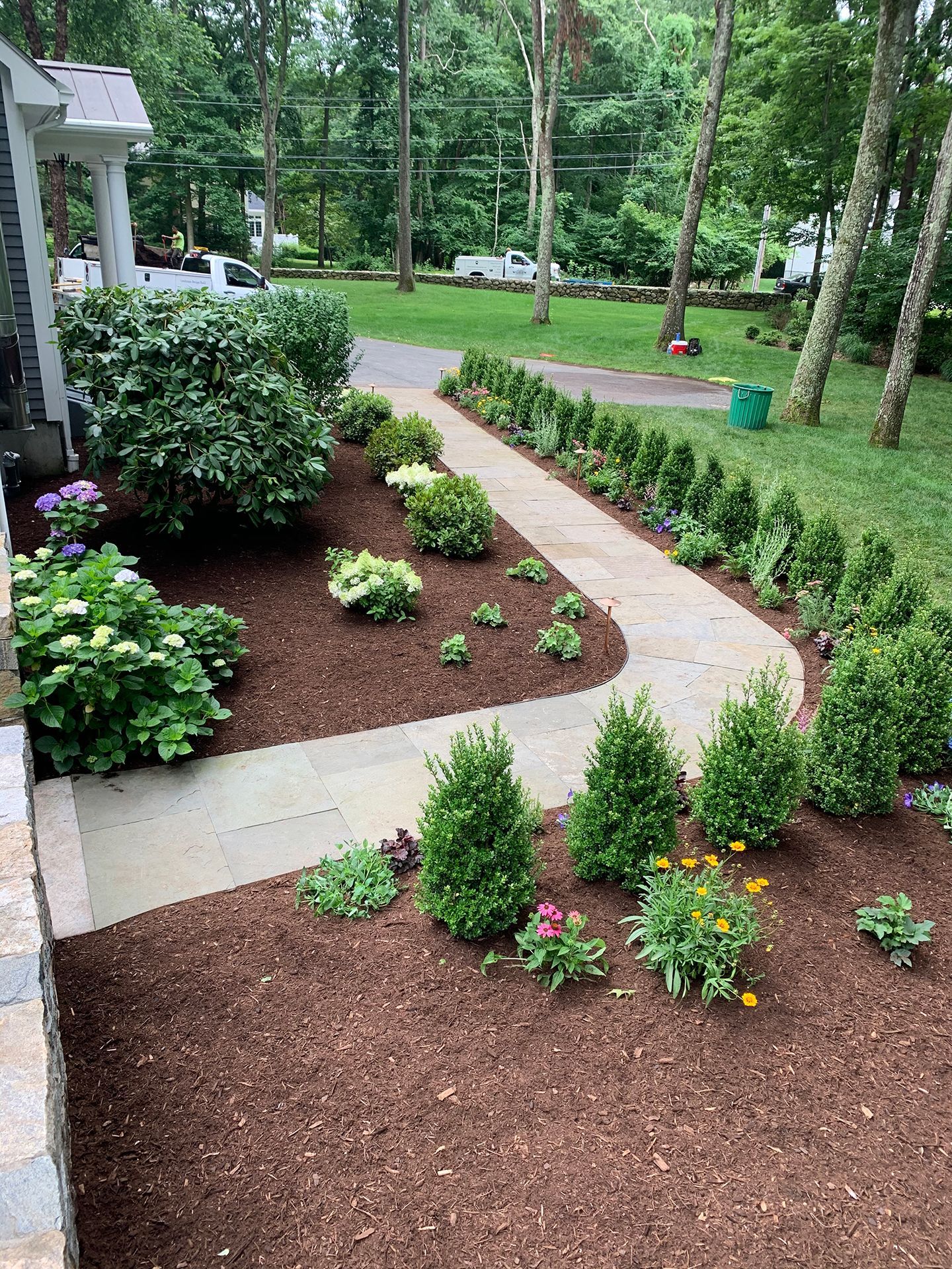 A walkway leading to a house surrounded by flowers and bushes.