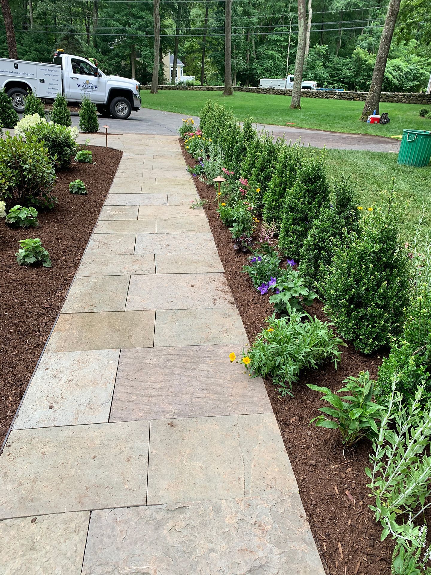 A white truck is parked on the side of the road next to a stone walkway.