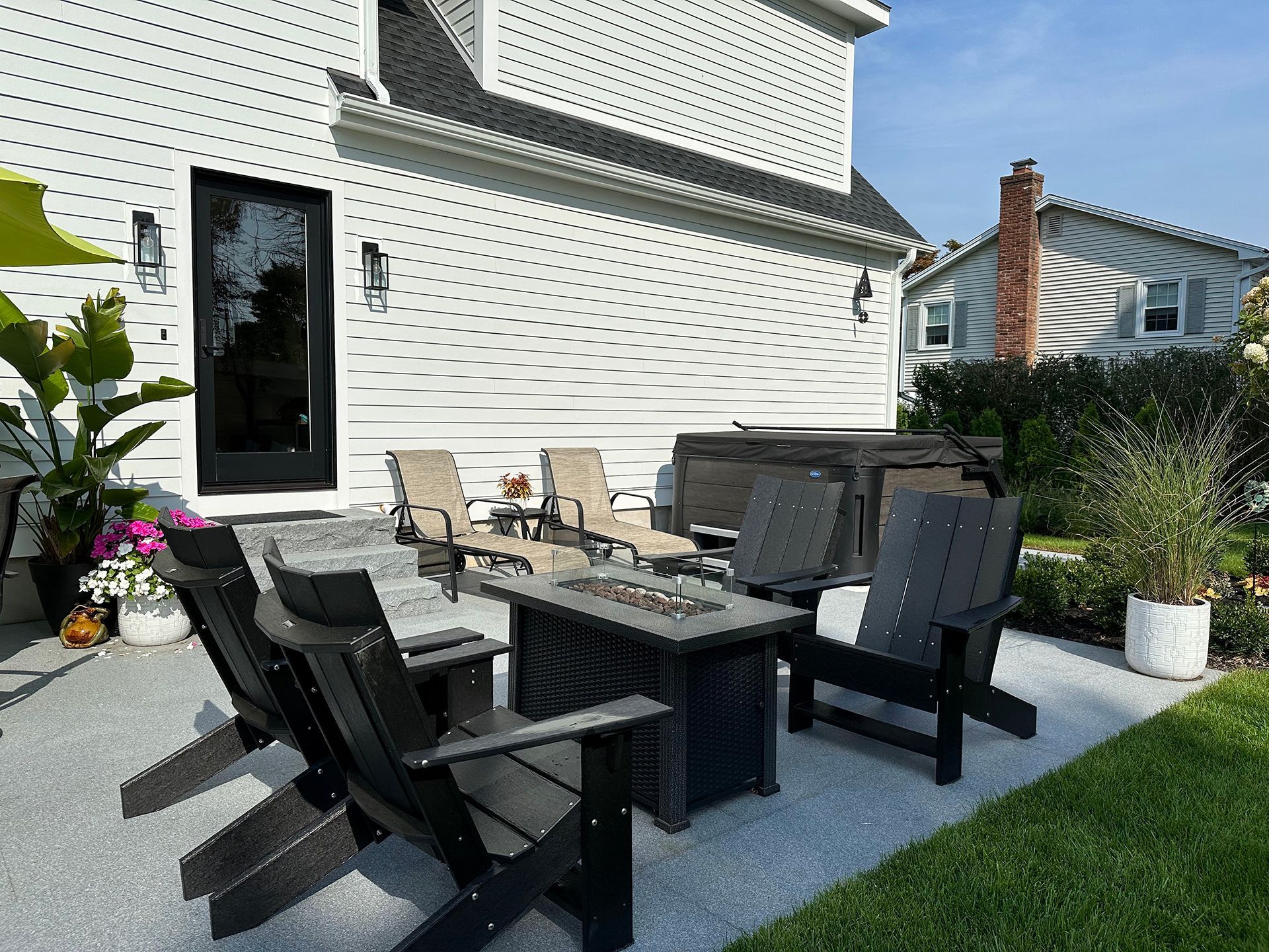 A patio with chairs, a table, and a fire pit in front of a house.