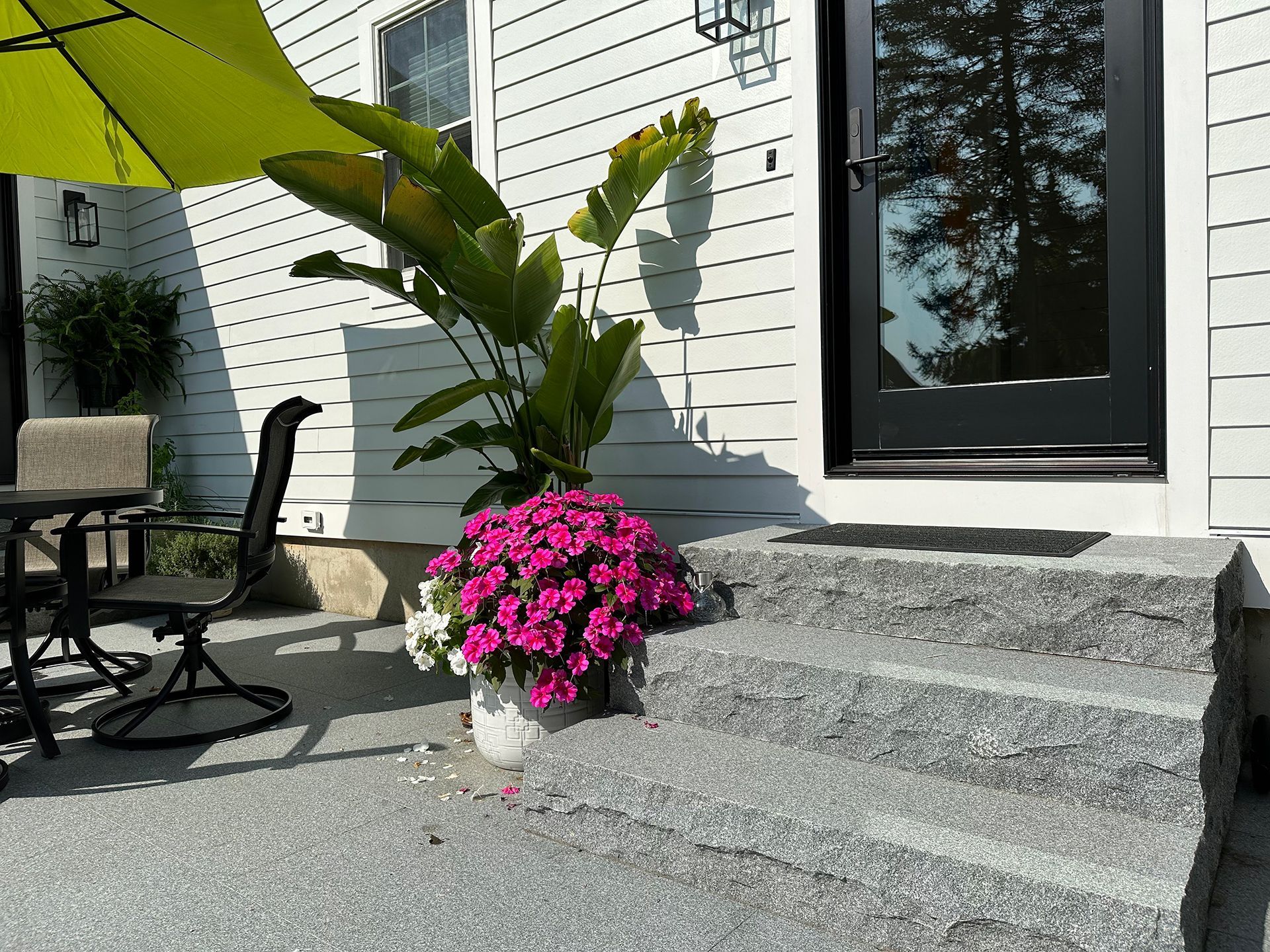 A patio with a table and chairs and a potted plant in front of a house.