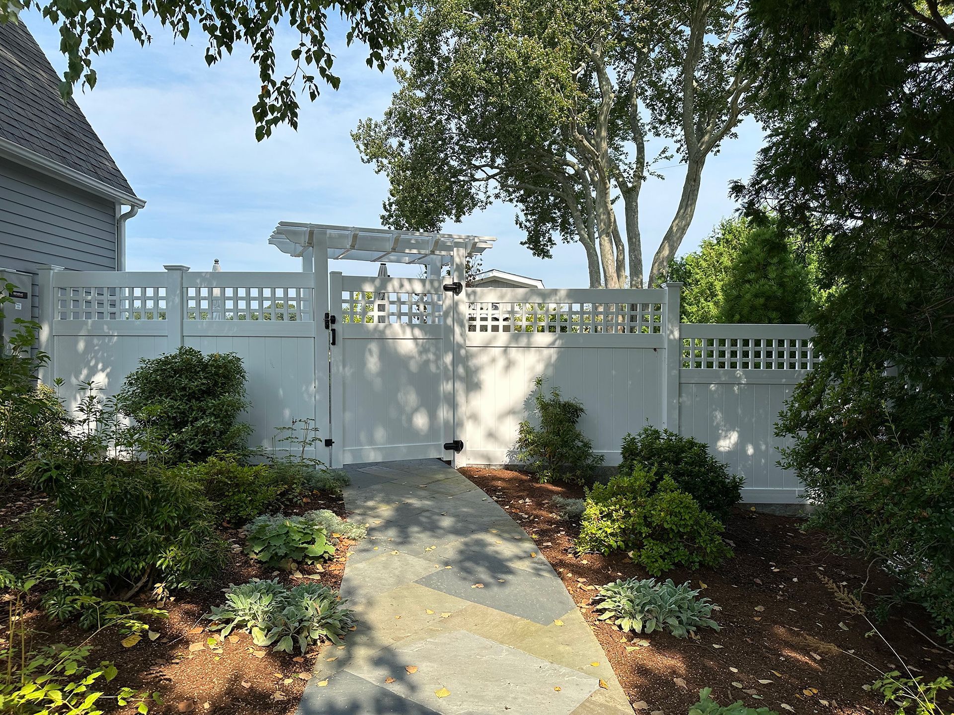 A white fence surrounds a stone walkway leading to a house.