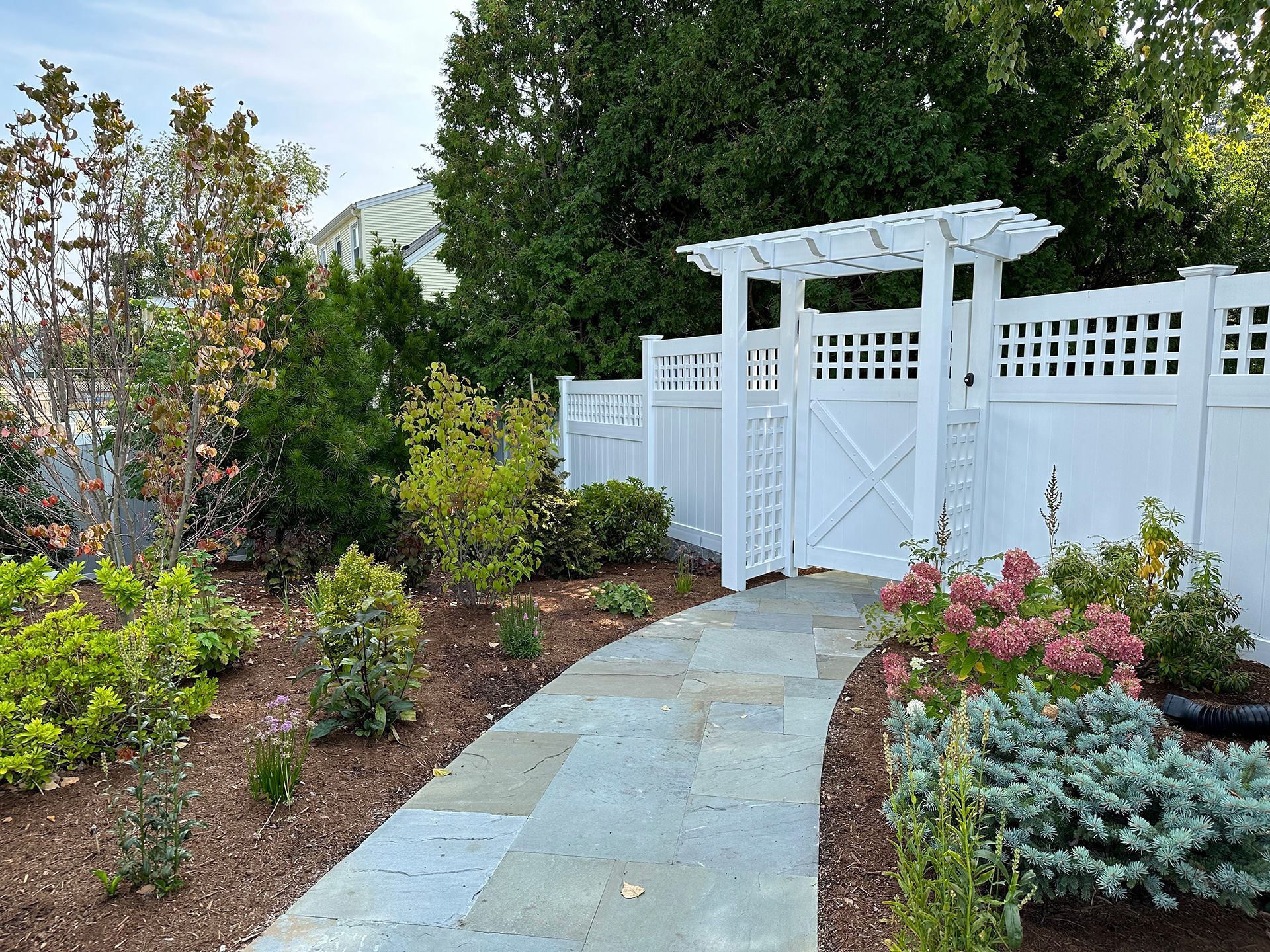A white fence surrounds a stone walkway leading to a gate.
